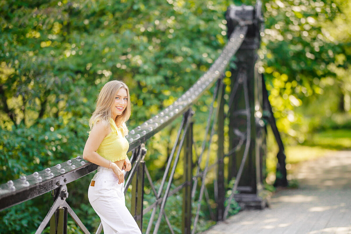 senior in the left corner leaning on victorian bridge smiling softly
