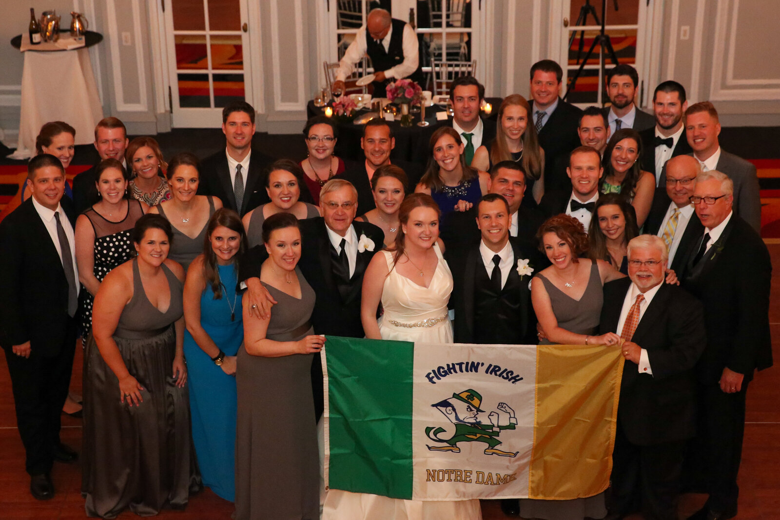 Bride and groom stand with their wedding guests holding University of Notre Dame flag