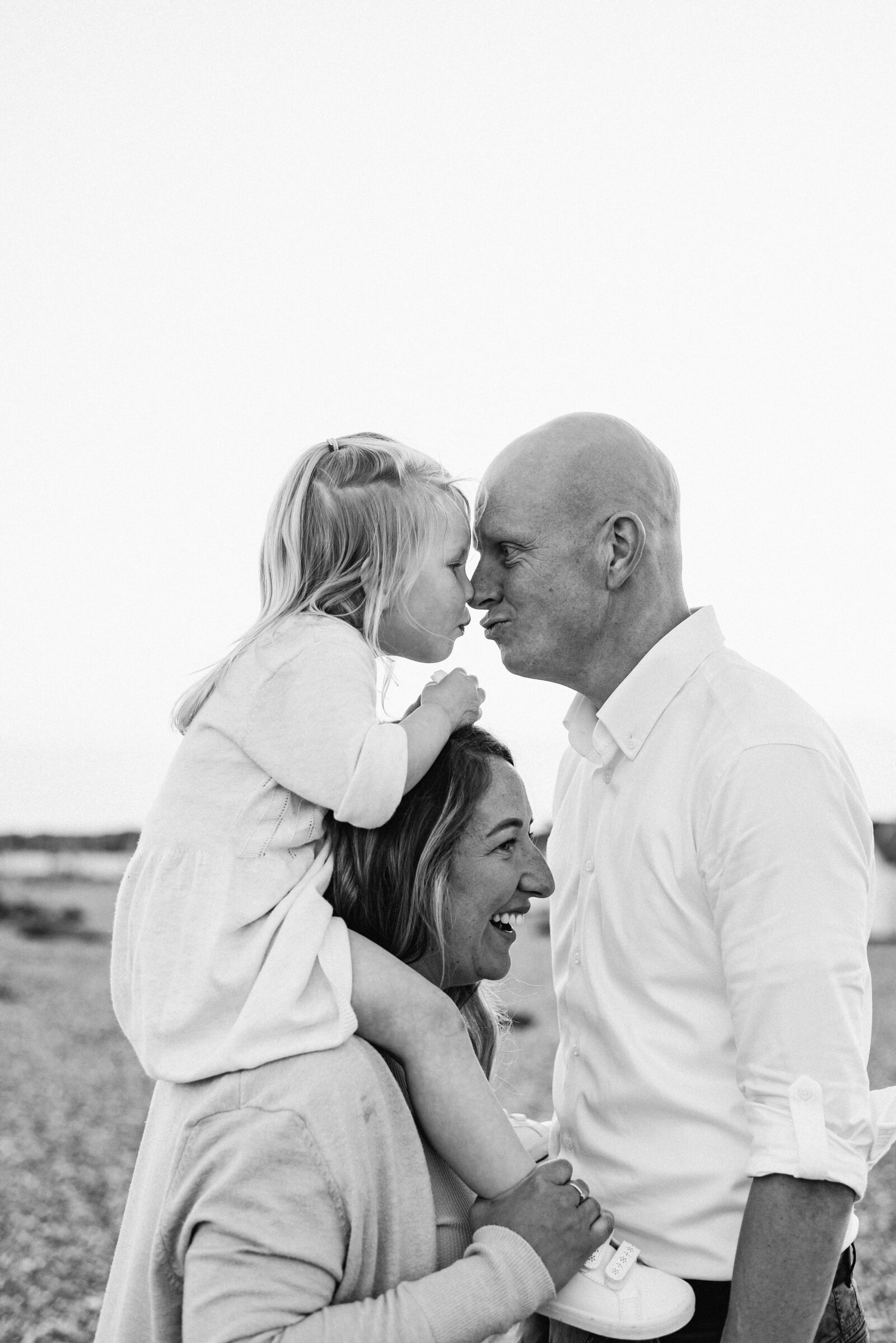 Little girl on mums sholders kissing dad at family photoshoot in goring west sussex