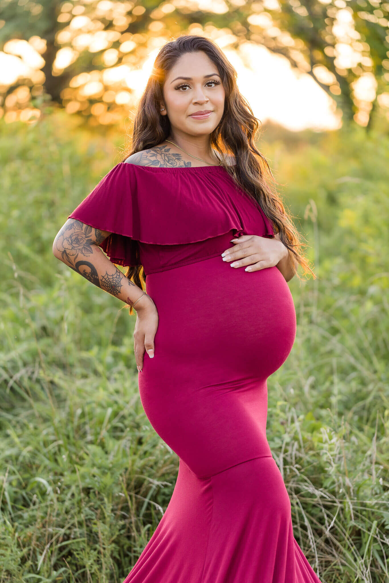 A pregnant woman in a red dress posing at a park in Northern Virginia at sunset.