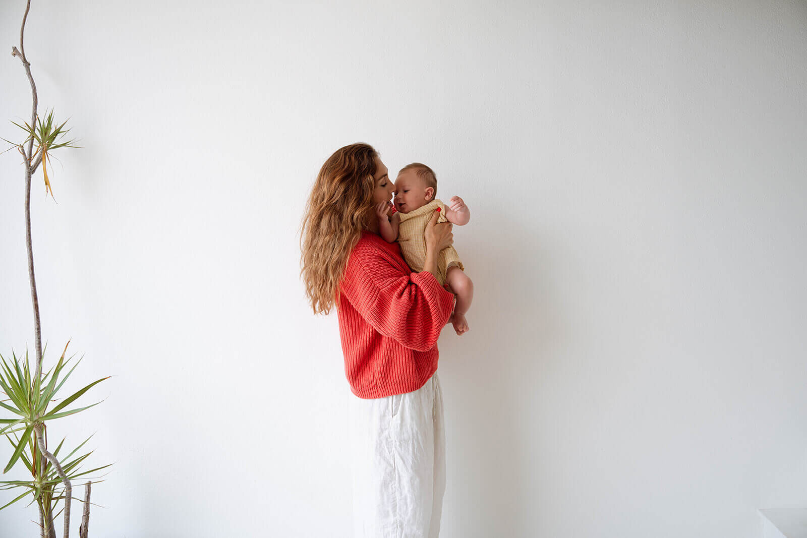 female wearing red sweater holding baby with yellow onesie in costa mesa studio