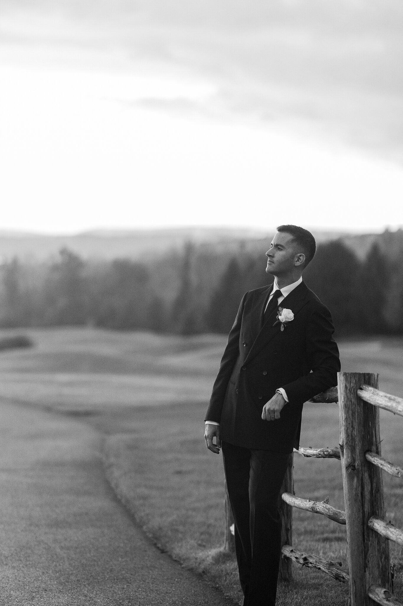  Groom casually leaning on wooden fence with scenic background at SkyView Golf Club