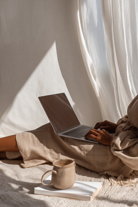 A designer’s hands typing on a laptop beside a coffee cup with the ocean in the background, symbolizing freedom, calm, and creativity at Kathalyst Design Studio.