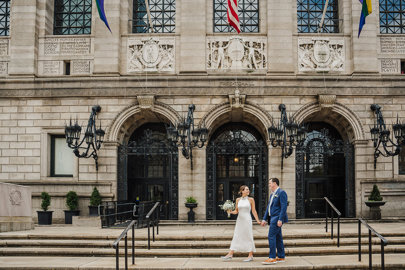 couple holds hands and walks in front of boston public library for elopement
