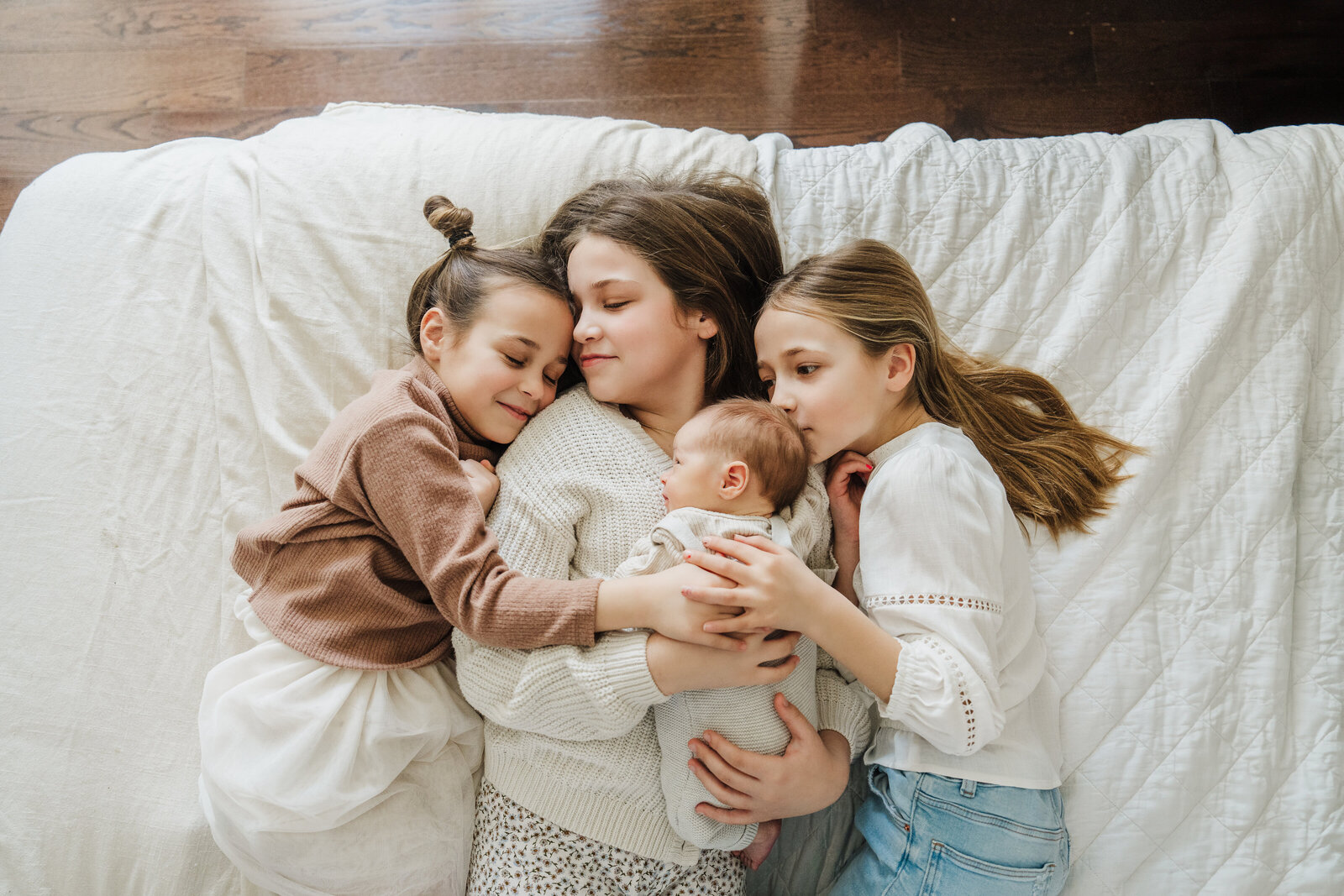 older sisters cradle baby brother on bed