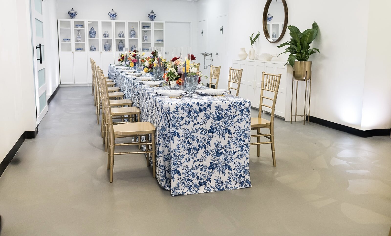 Styled table setup at The Parlor at Wells in Memphis, featuring vibrant floral centerpieces, blue toile linens, gold chairs, and natural light—ideal for showers, workshops, and private dinners.