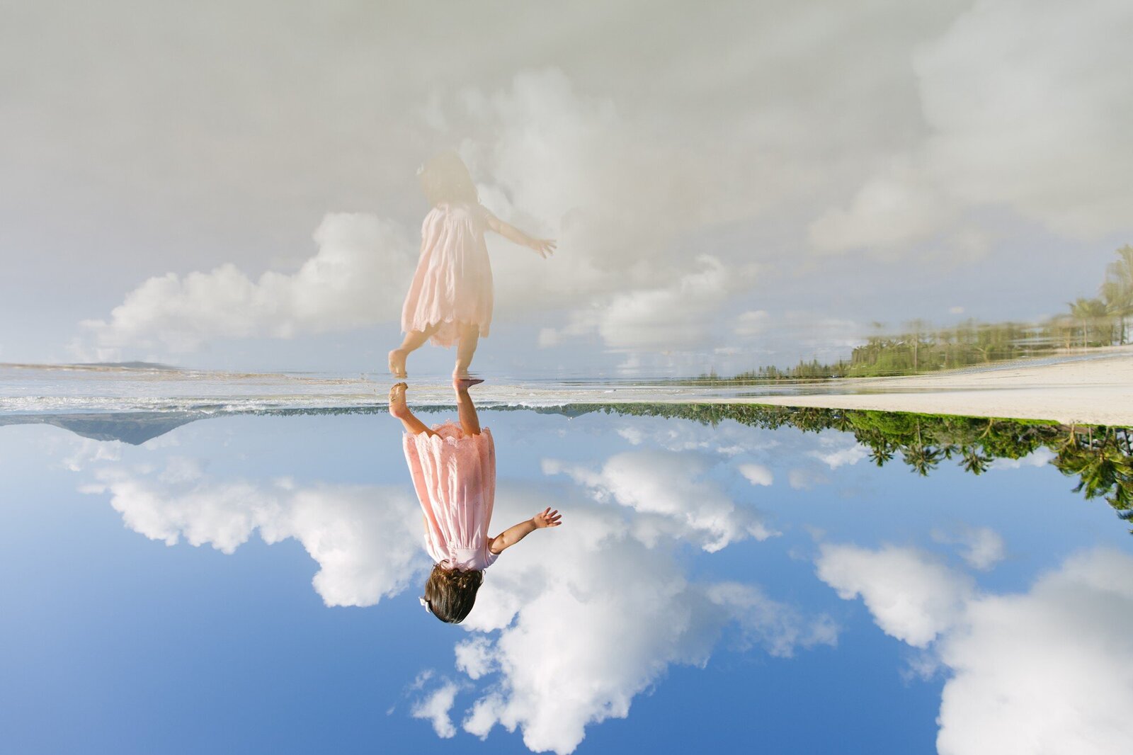 a toddler in pink runs on the shore at kailua beach with her reflection in the calm water