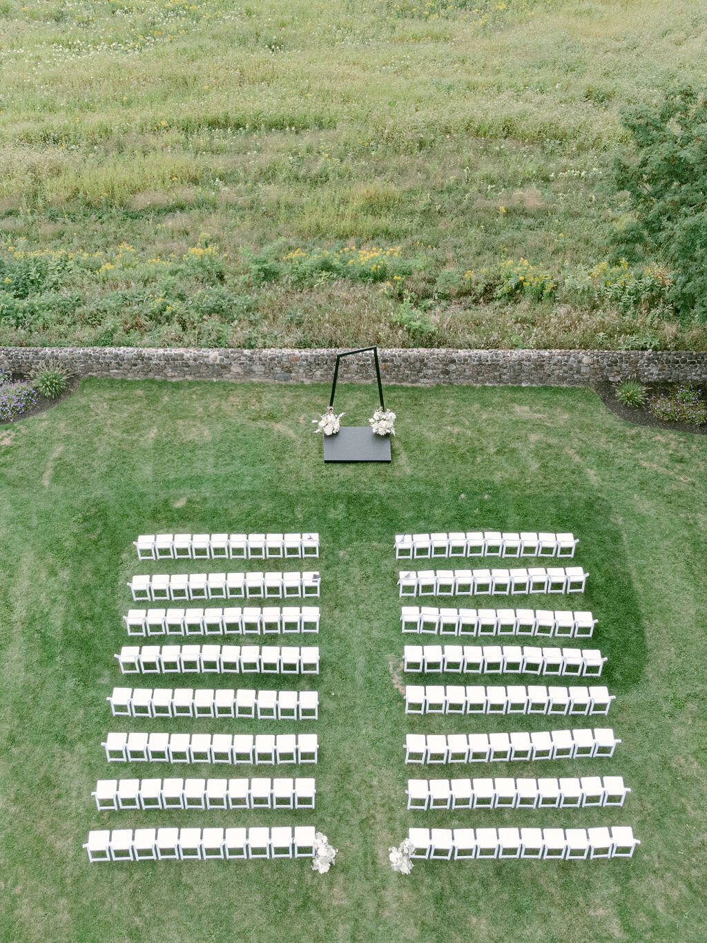 birds eye view of white ceremony shairs facing a modern black arch in front of a stone wall at Windridge