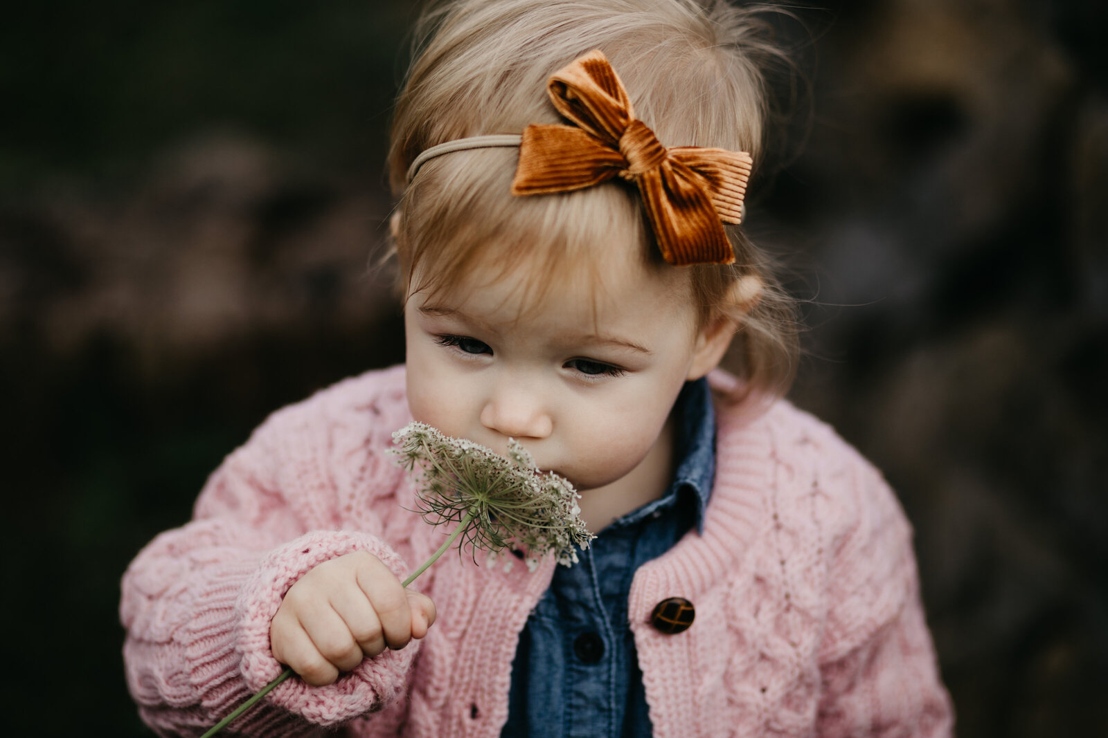 A little girl in an orange bow smells a flower
