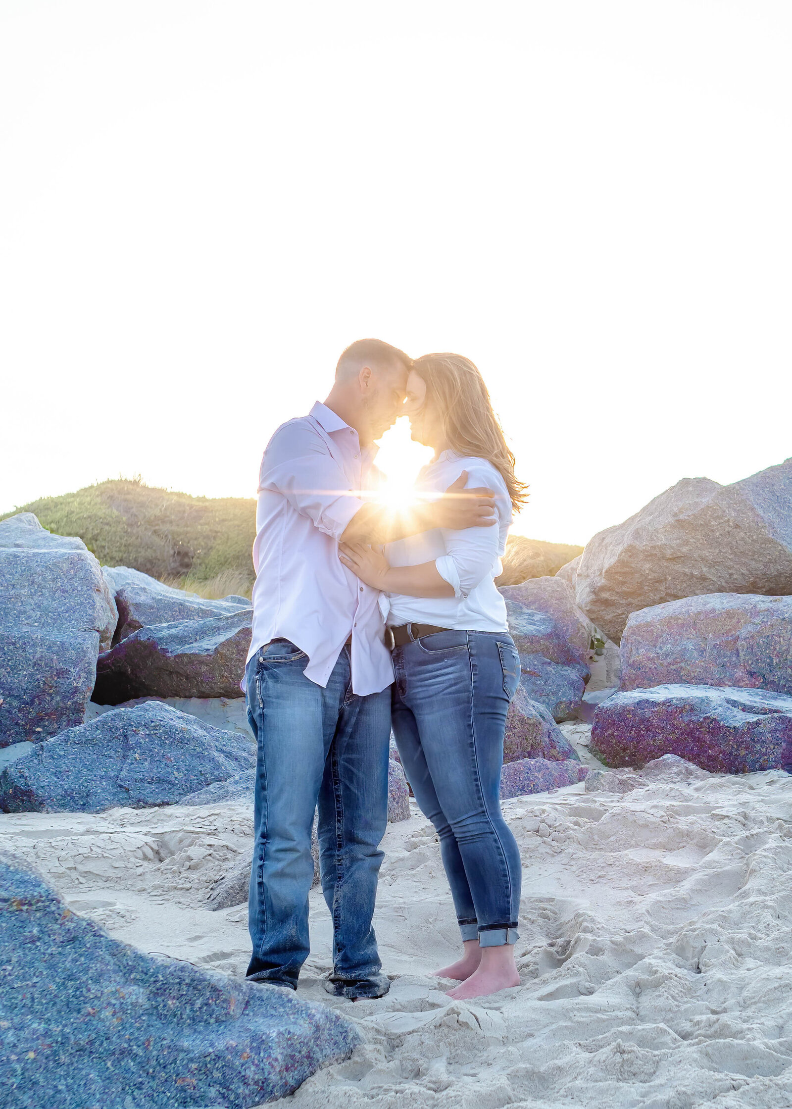 An engaged couple embracing on the beach in Wilmington, NC, with the sun shining through their clasped hands. This romantic moment captures the essence of authentic wedding photography, perfect for couples seeking an artistic wedding photographer in North Carolina.