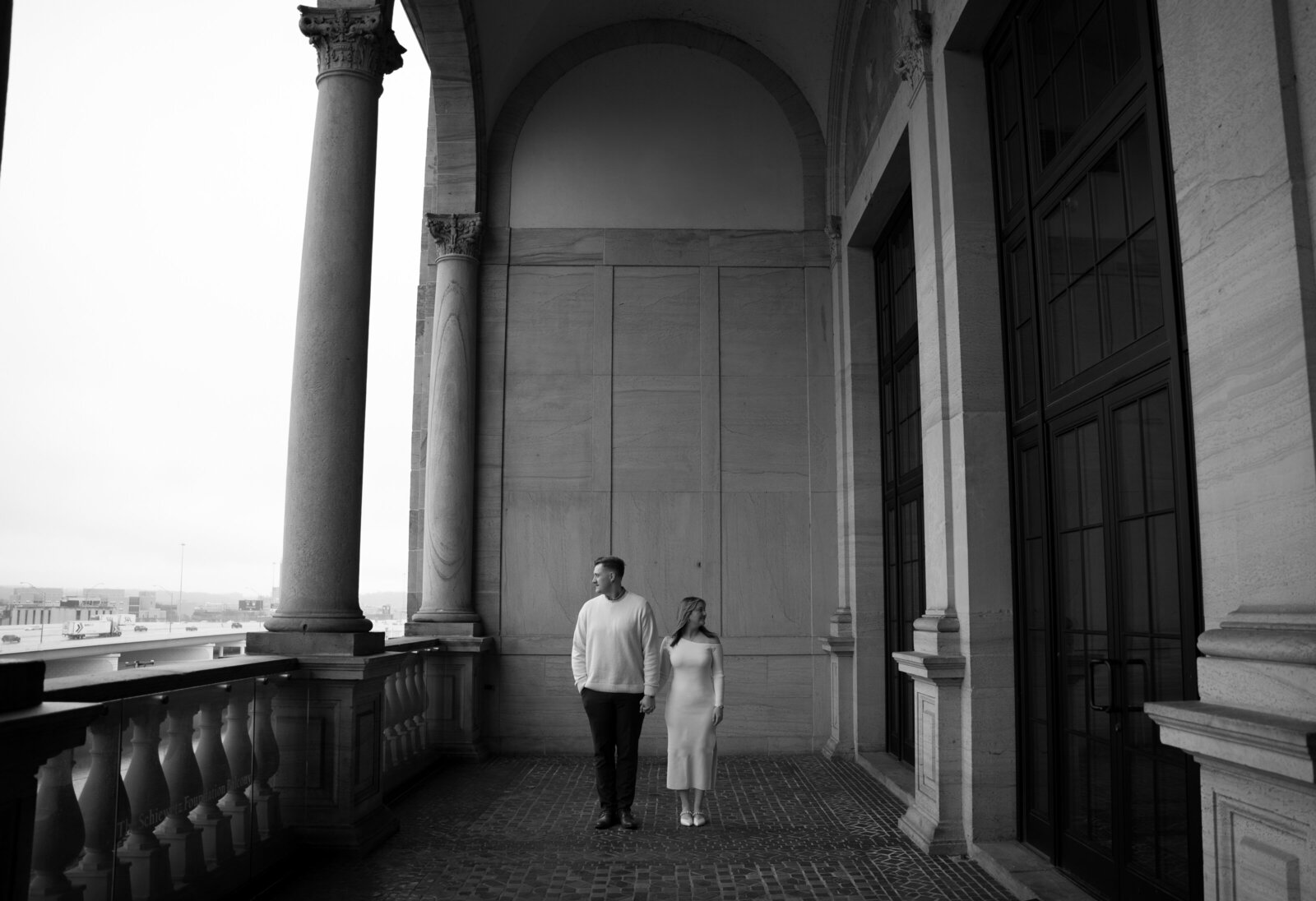 A couple standing on a balcony at an art museum for their engagement announcement photos.