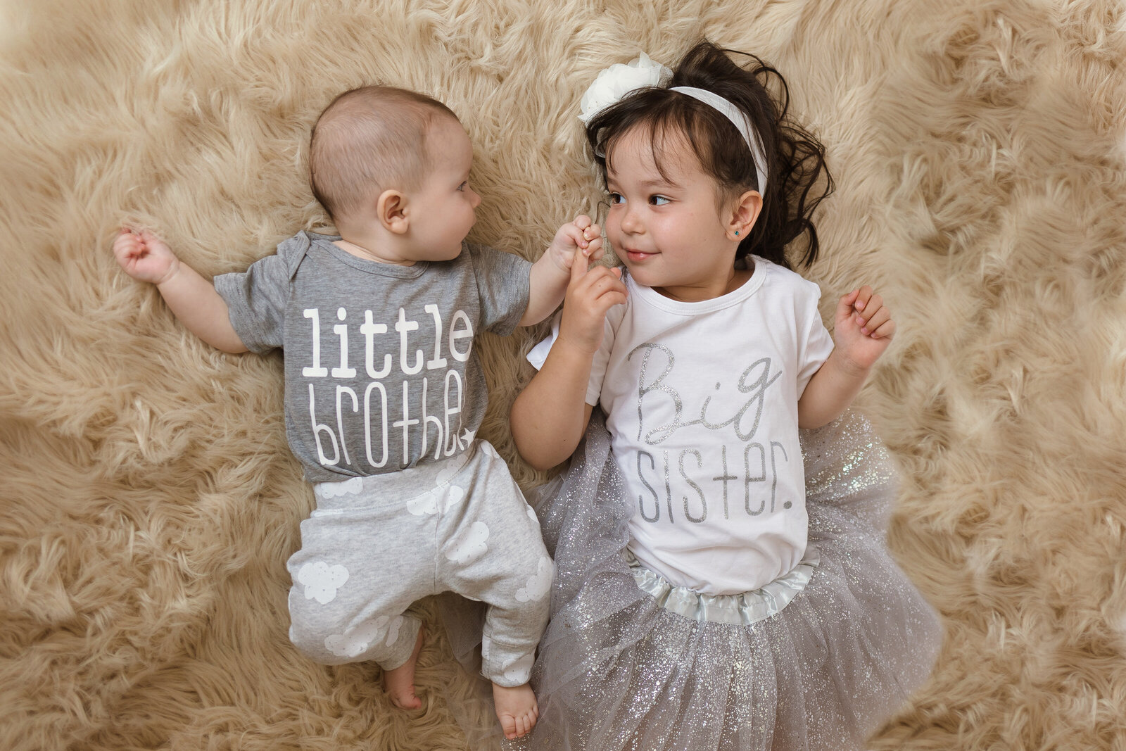Milestone Photographer, a baby boy and his little sister lay beside each other with shirts that read "little brother" and "big sister"