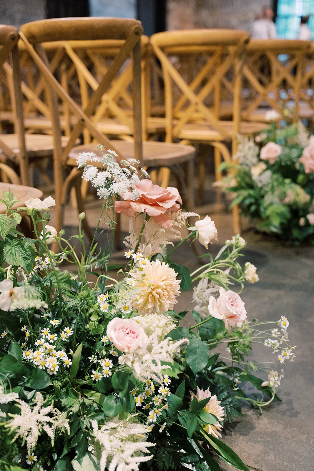 Close-up of floral aisle meadow arrangement with lush greenery, queen anns lace, blush and pink garden roses, daisies, white astilbe and tan dahlias.