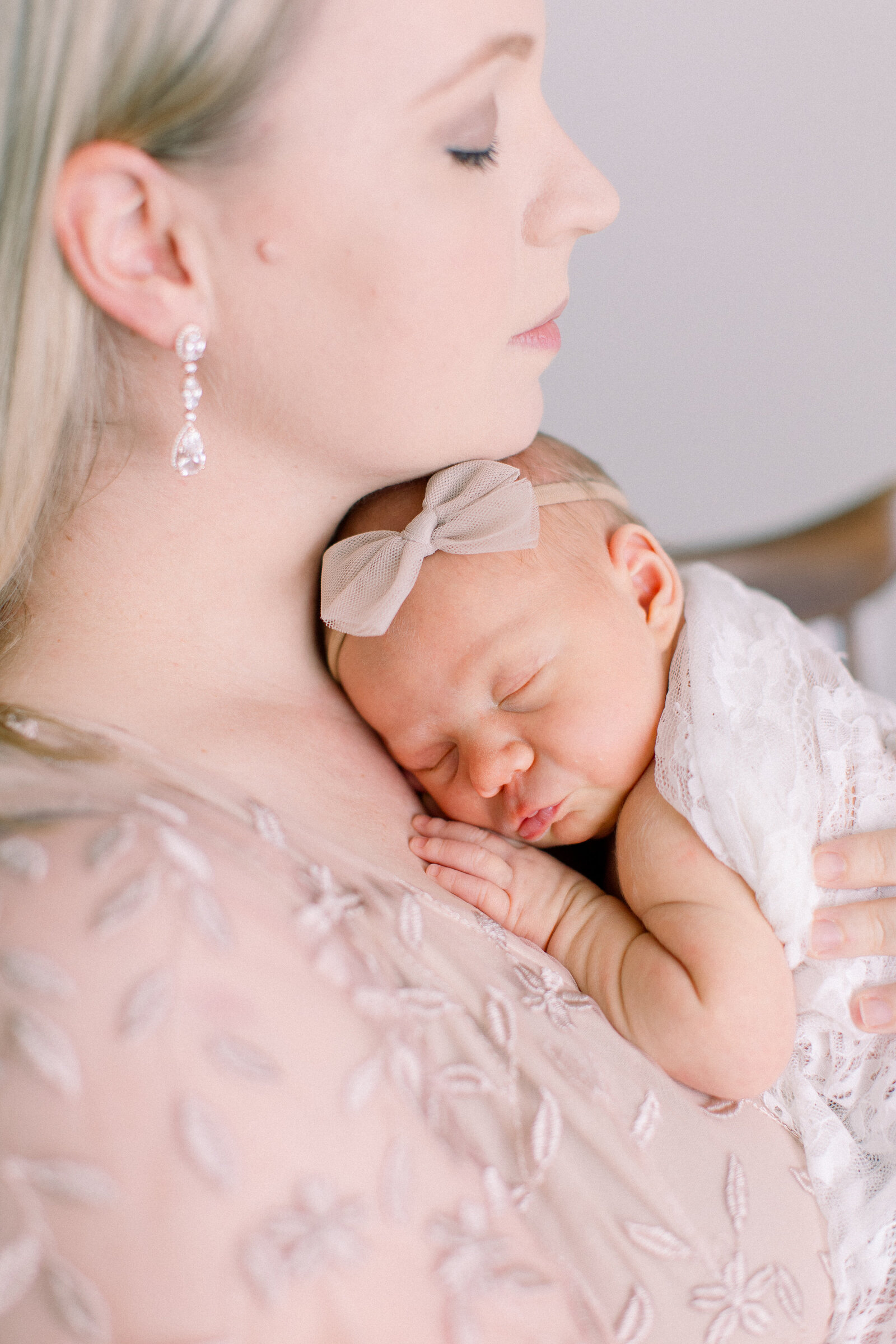 Serene motherhood portrait of a mom in a lace gown, snuggling her sleeping baby wrapped in lace on her chest tucked under her chin by NH newborn photographer Fieldstone Studio.