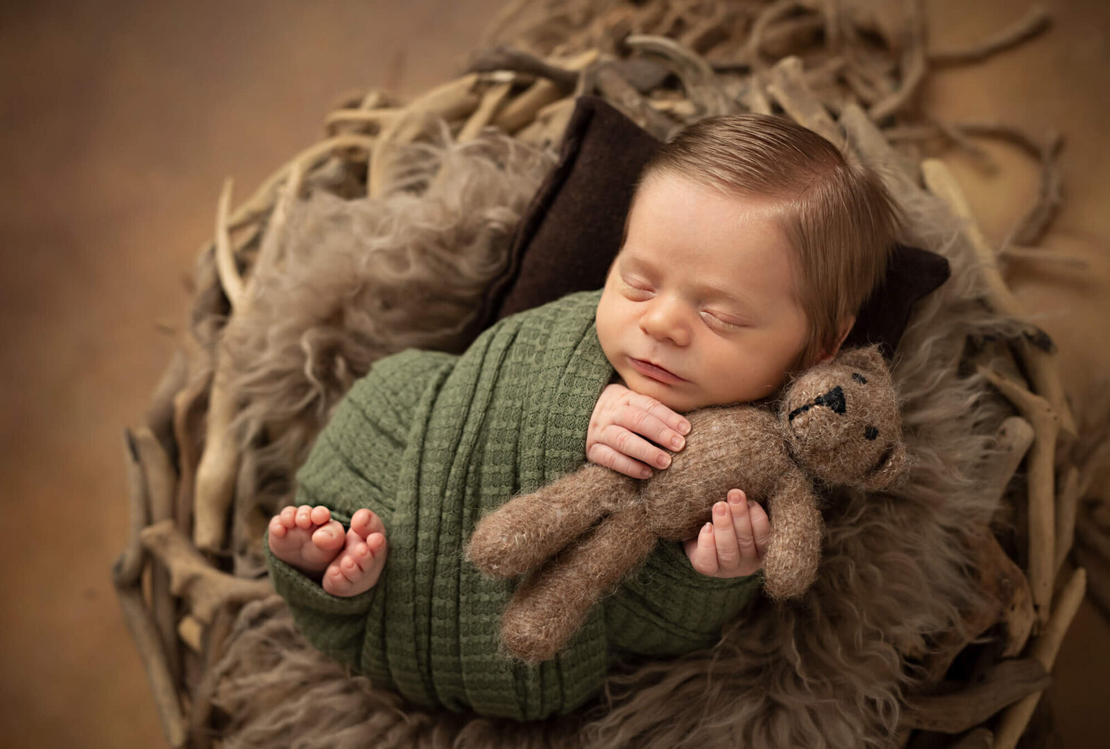 10 day old baby boy in a nest with green wrap and teddy bear