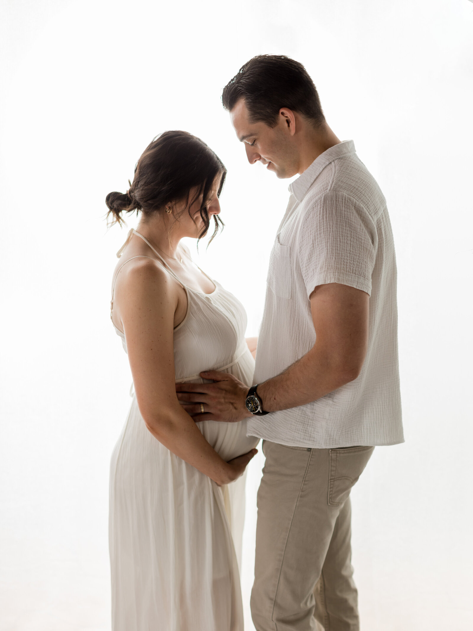 husband and wife in white maternity dress holding baby bump for maternity photoshoot
