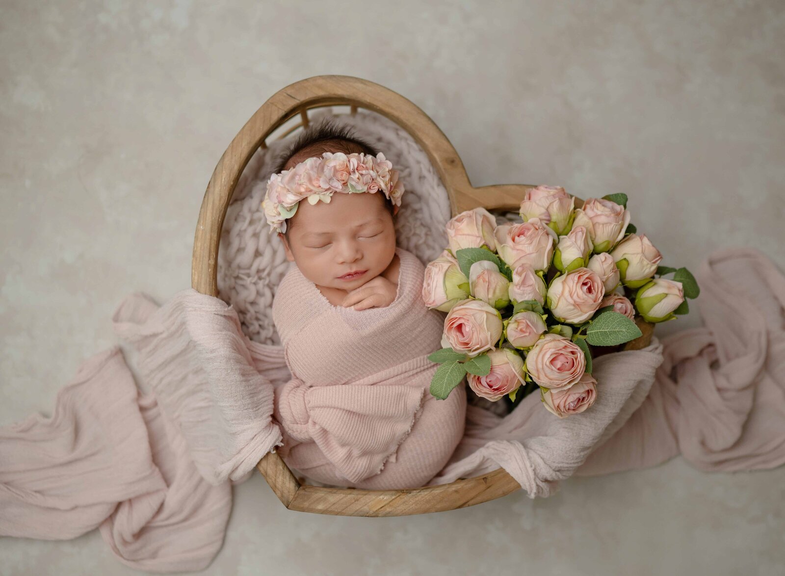 Baby girl swaddled in pink wrap placed in a heart crate with peach roses/