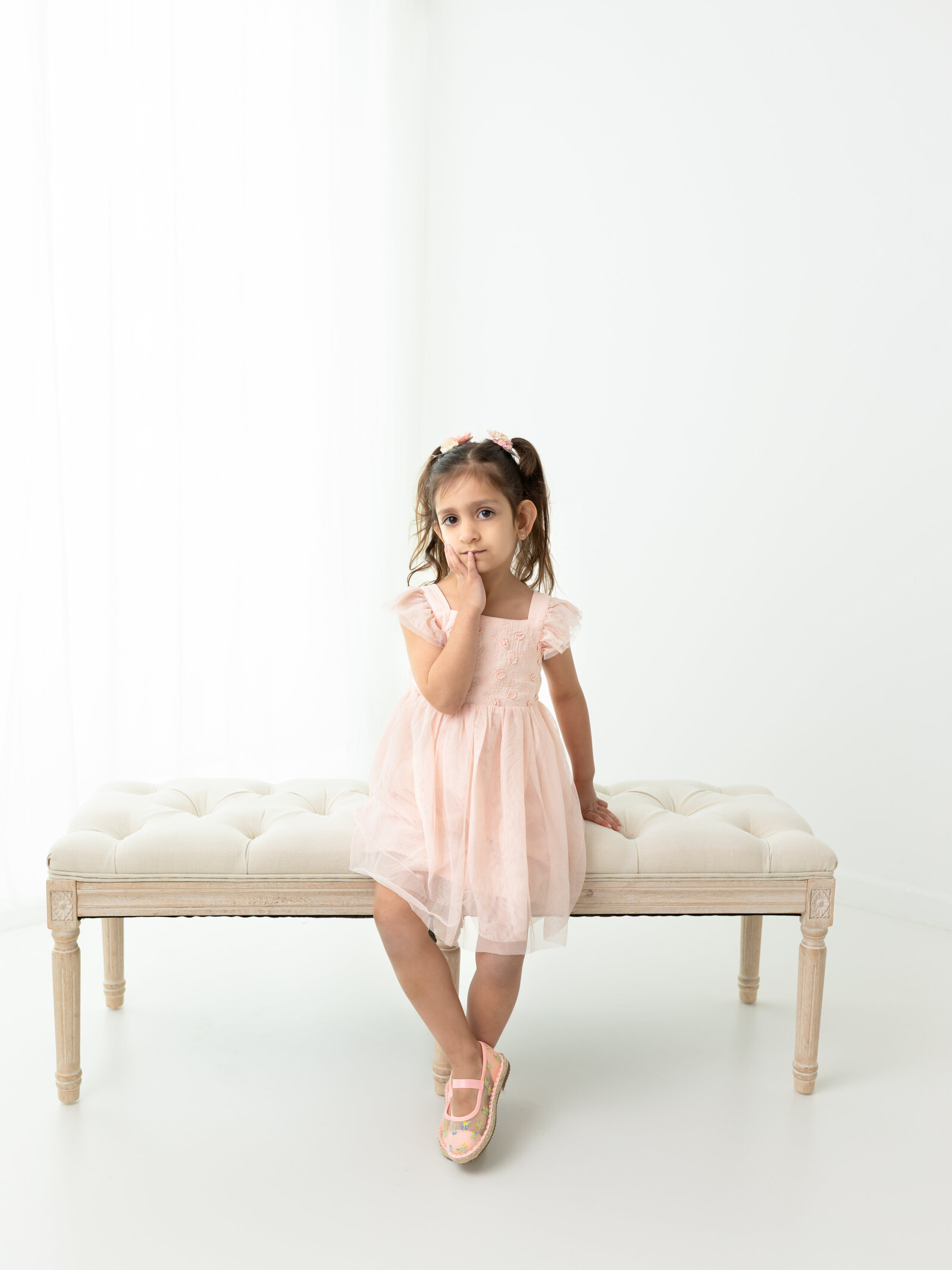 little girl in pink dress sitting on bench for white studio portraits