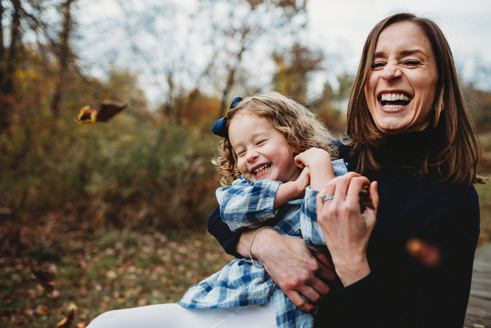 mom and daughter laugh playing in leaves in fall photo