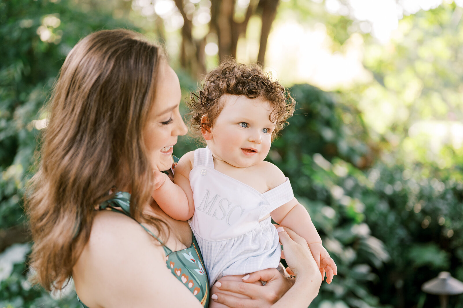 Mom in green dress holds baby boy with curly hair during outdoor family session in Raleigh, North Carolina