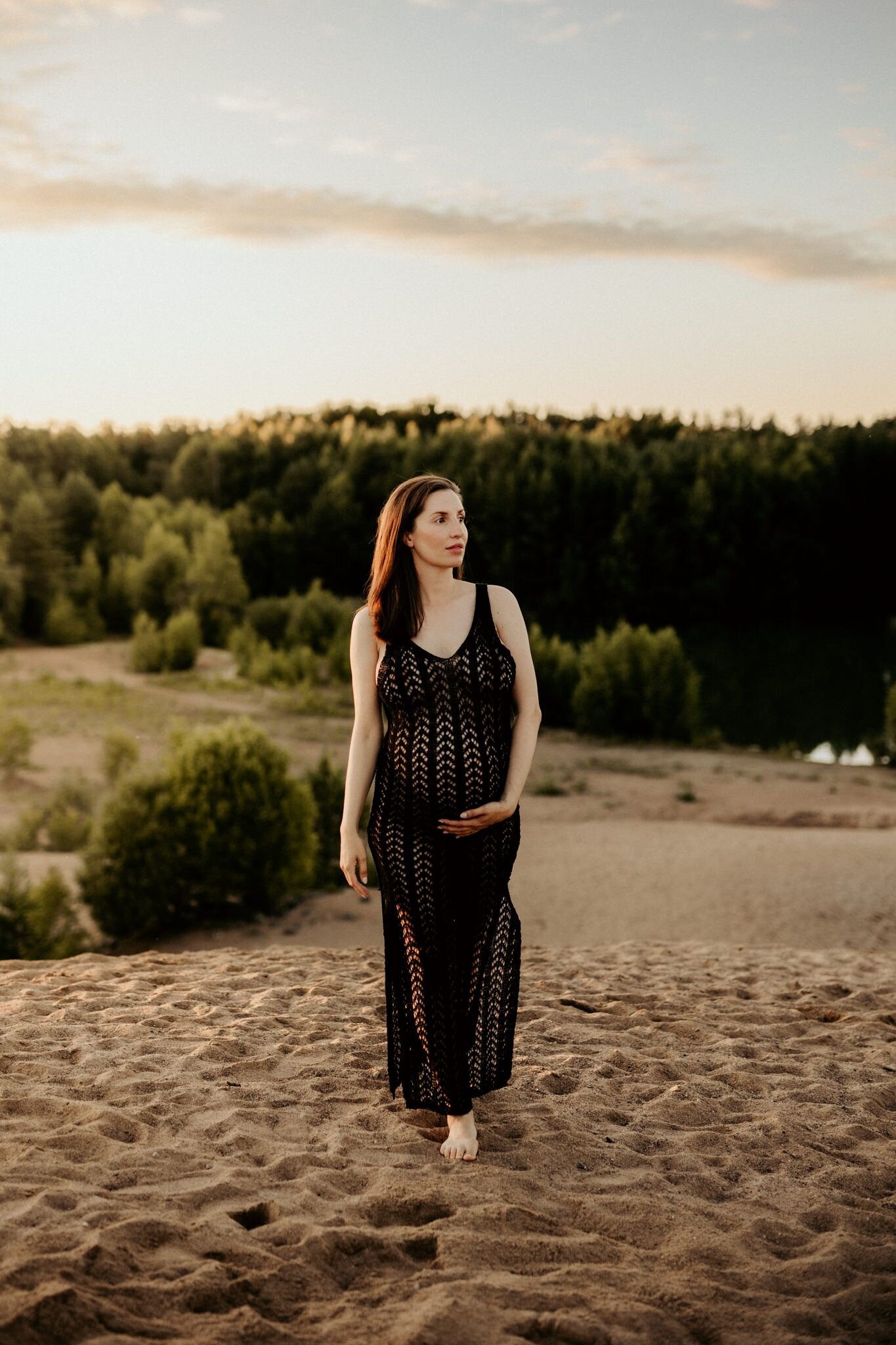 en gravid kvinna går i ett sandtäckt landskap iklädd en virkad klänning