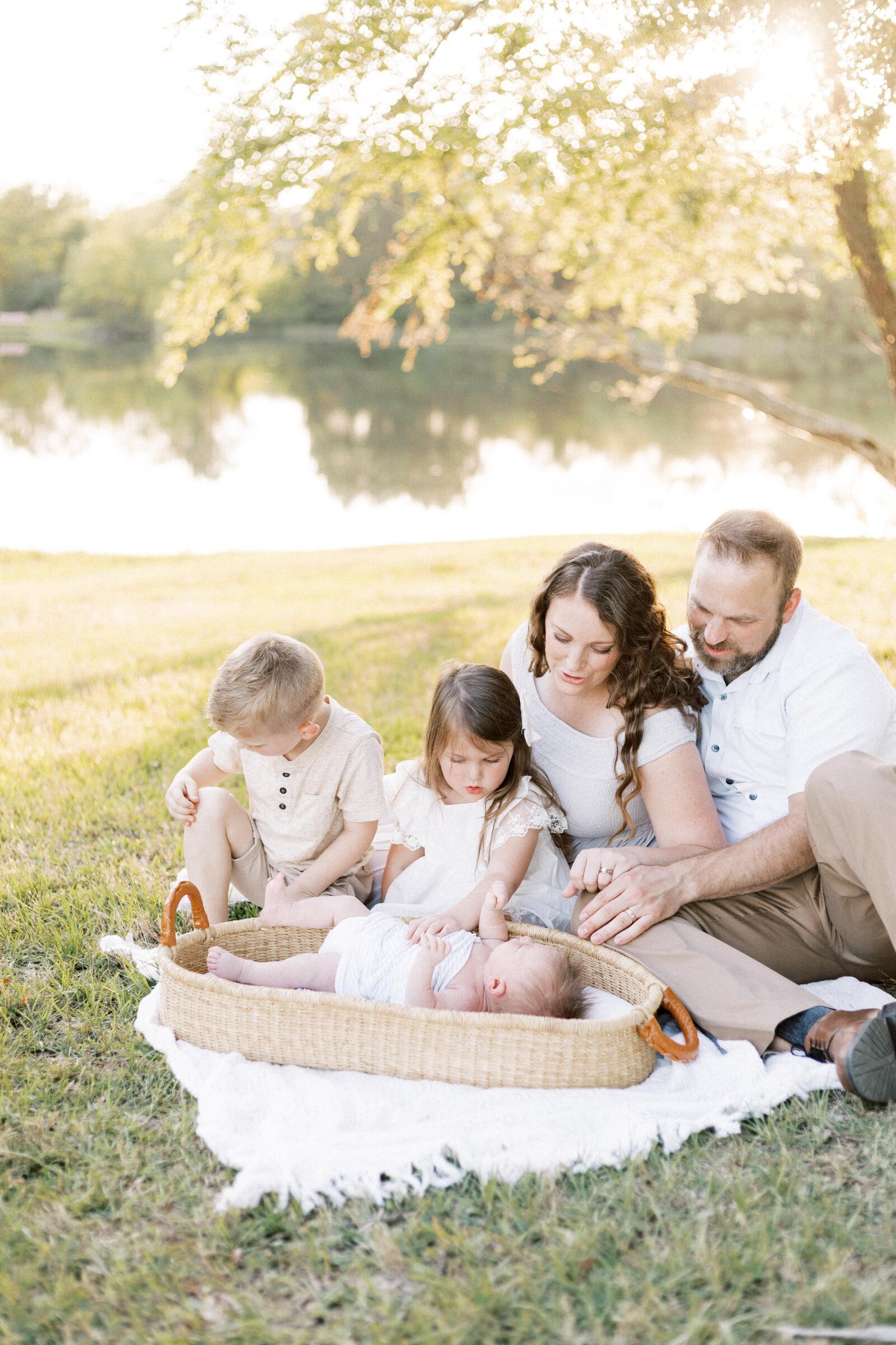 family sitting by lake and looking at baby in basket in peoria illinois newborn photos 