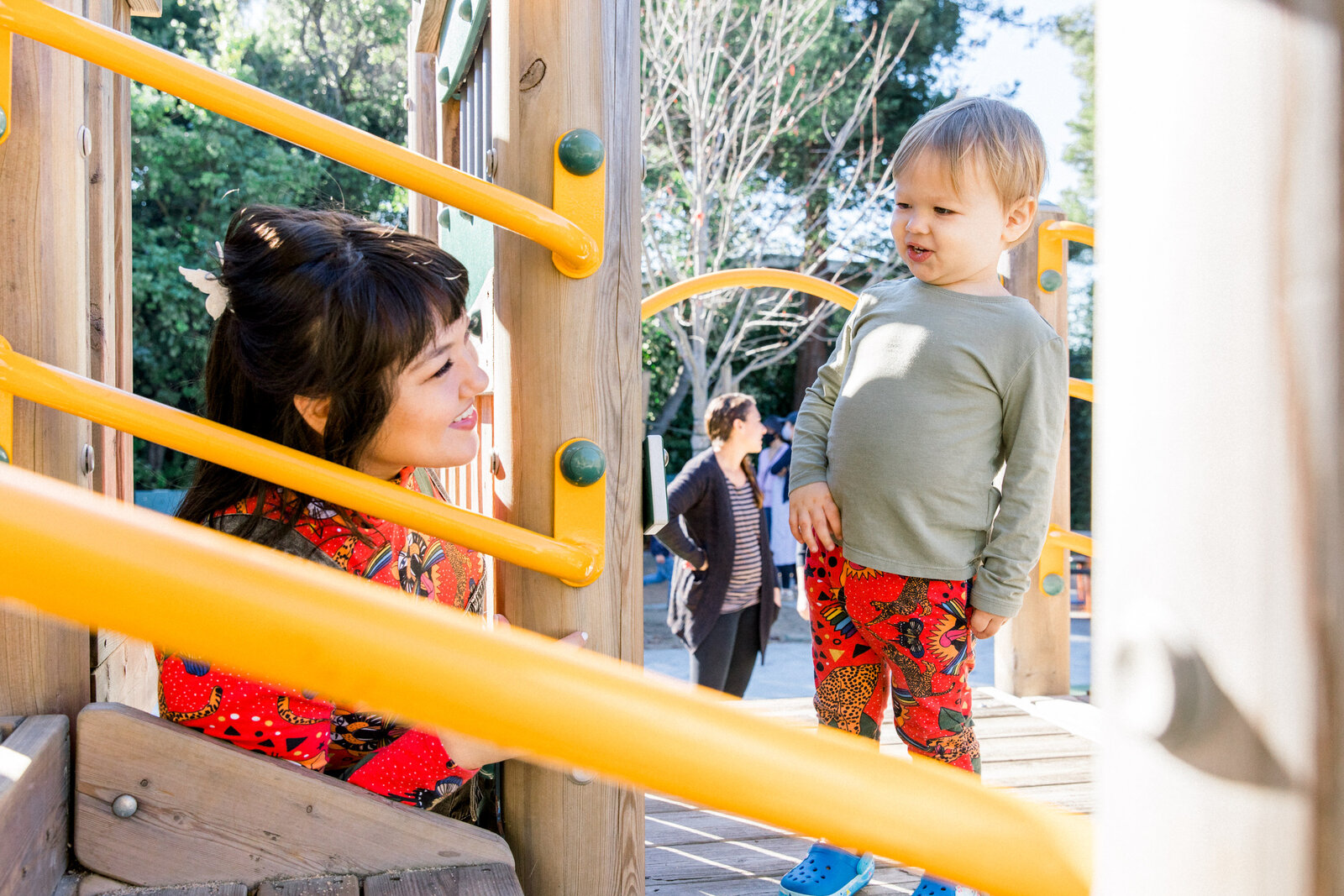 Asian mom playing peekaboo with toddler son at a playground in berkeley california