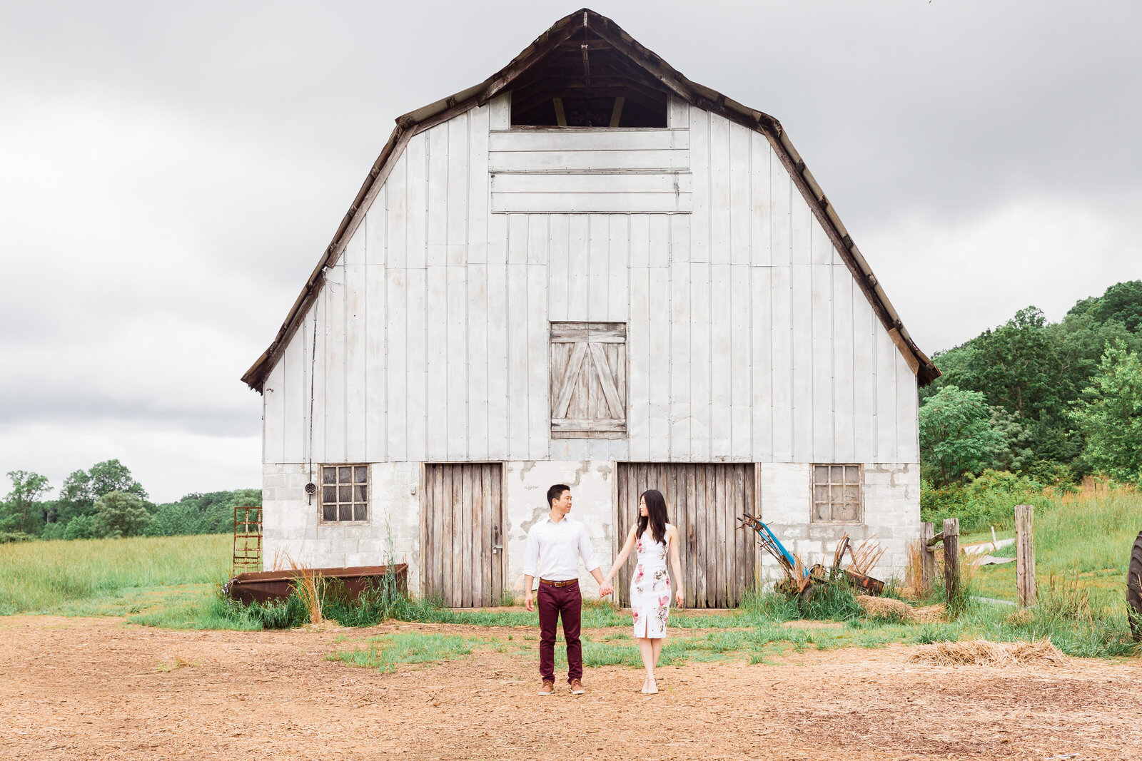 Couple holding hands in front of a white barn house
