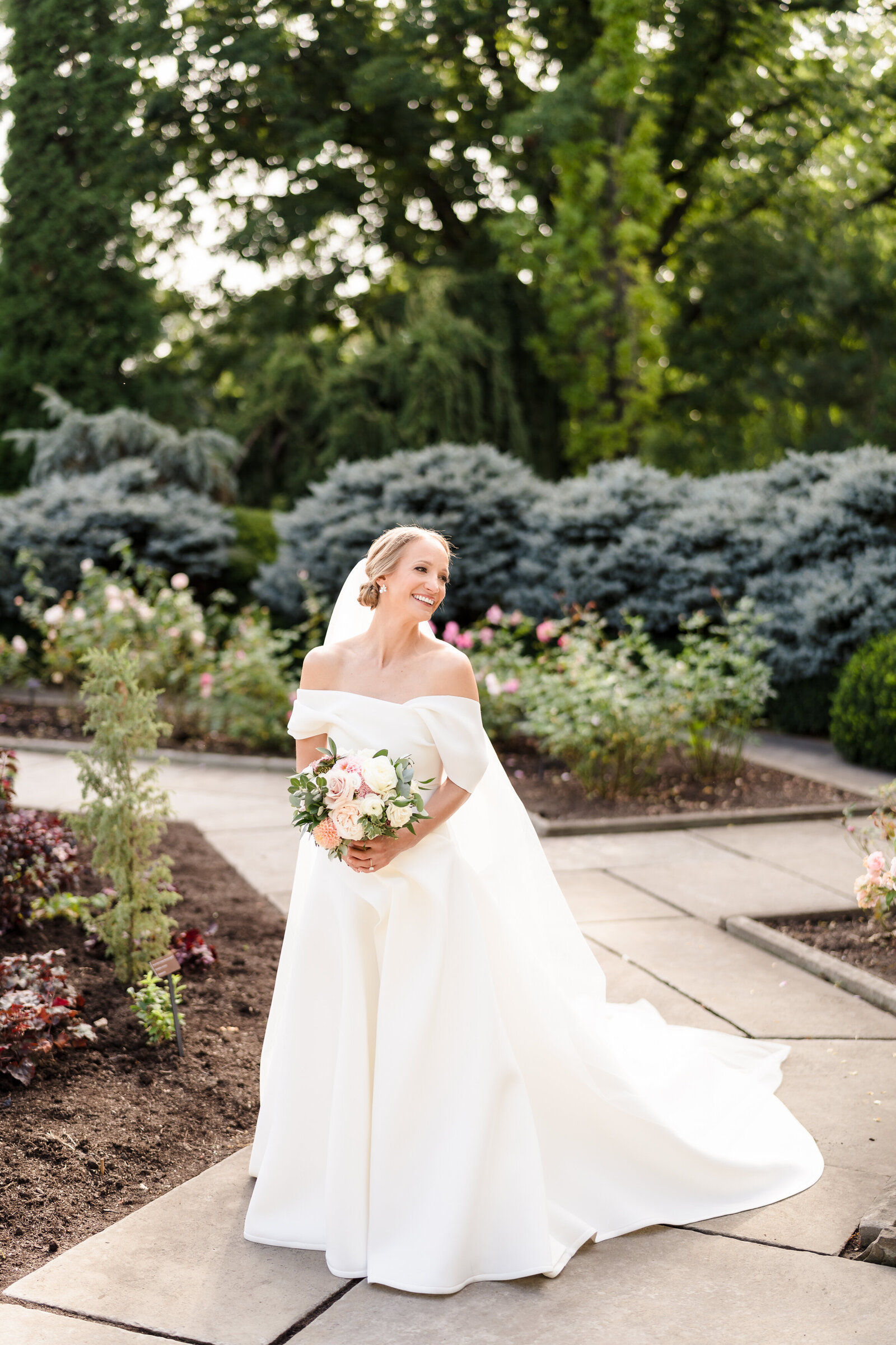A bride in a flowing white wedding dress smiles and looks to the side at the Cleveland Botanical Gardens