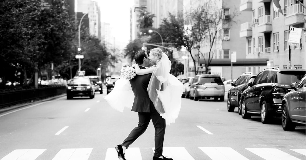 black and white image of groom carrying  bride across Park Avenue in NYC