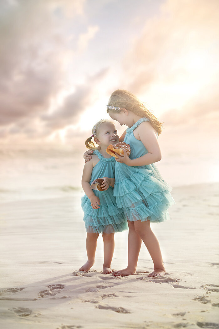 Siblings hugging on the beach holding sea shells, Dallas family photographer.
