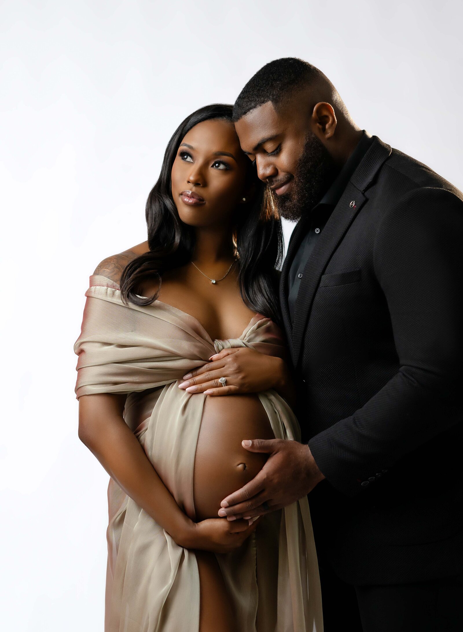Mom wrapped in gold drape and Dad holding baby belly. Photographed at Atlanta Maternity photo studio.