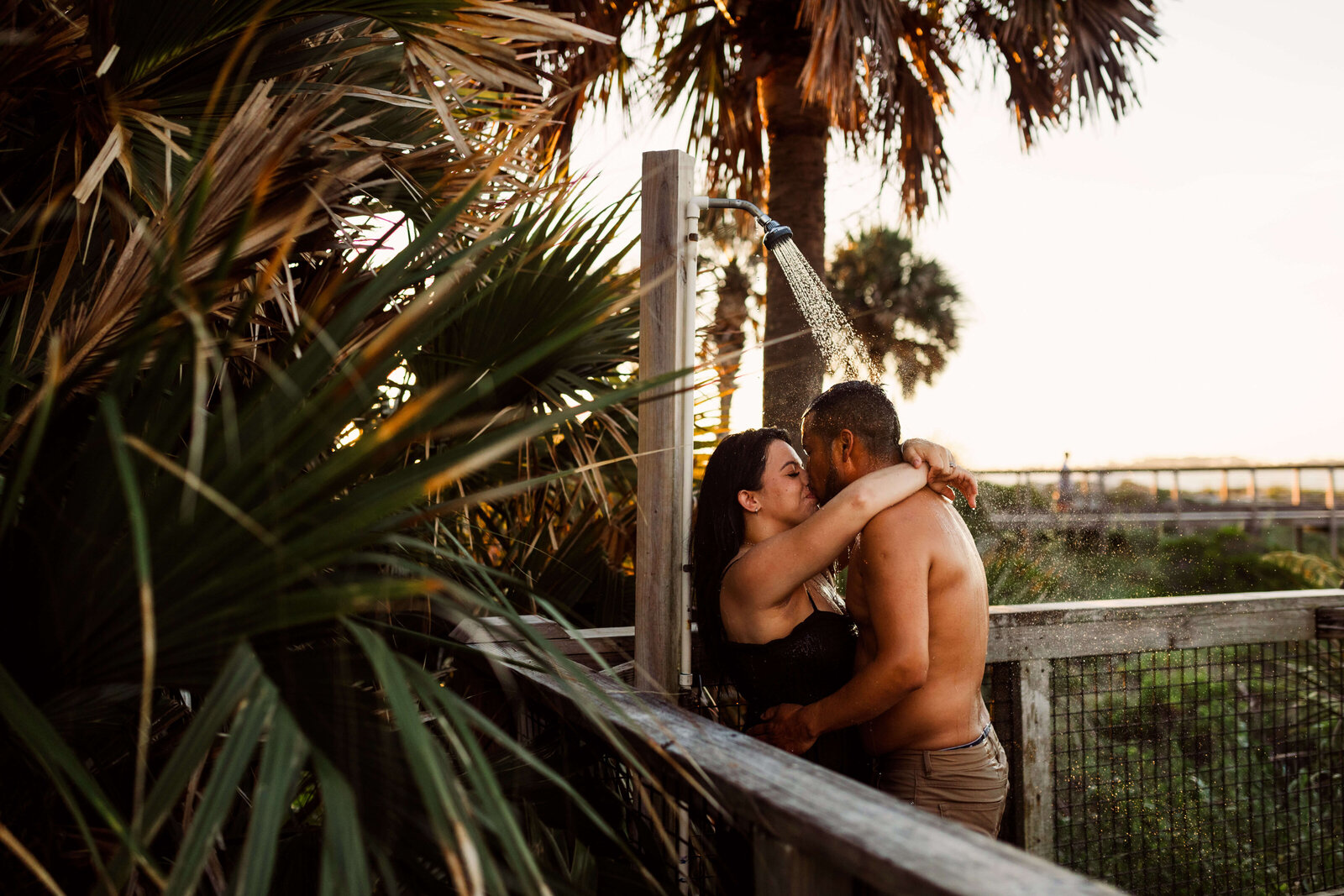 married couple kisses under beach shower in St. Andrews State Park -after intimate sunrise session with photographer Brittney Stanley of Be Seen Photos