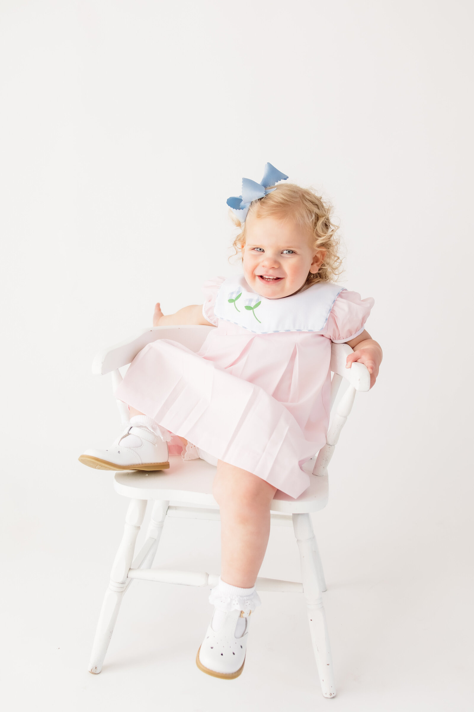 Little girl lounging on a white chair and smiling at the camera