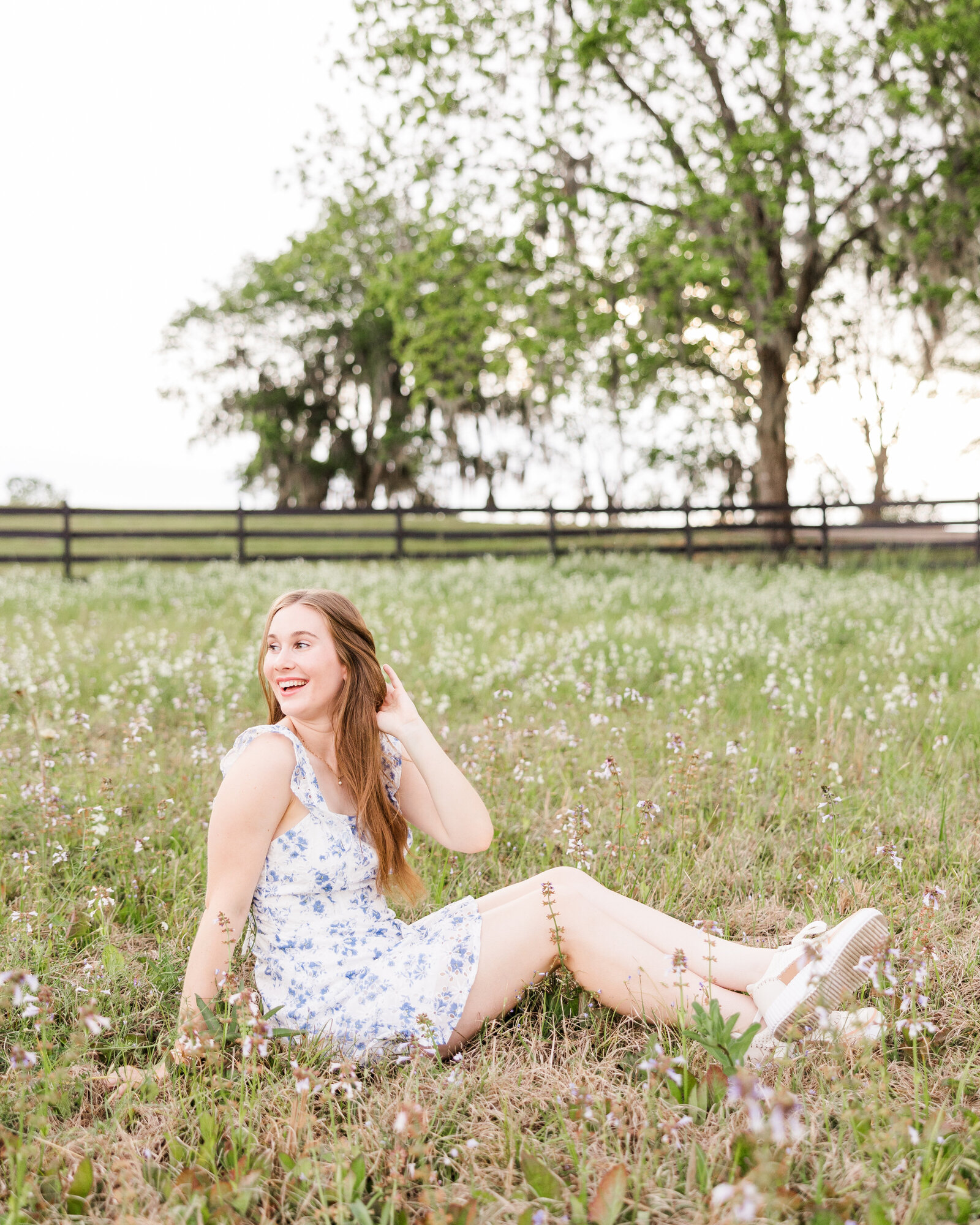 Sophie sitting in a field surrounded by wildflowers, smiling joyfully, captured by Abby Bell Photography, Fine Art Portrait Photographer based in Alabama.