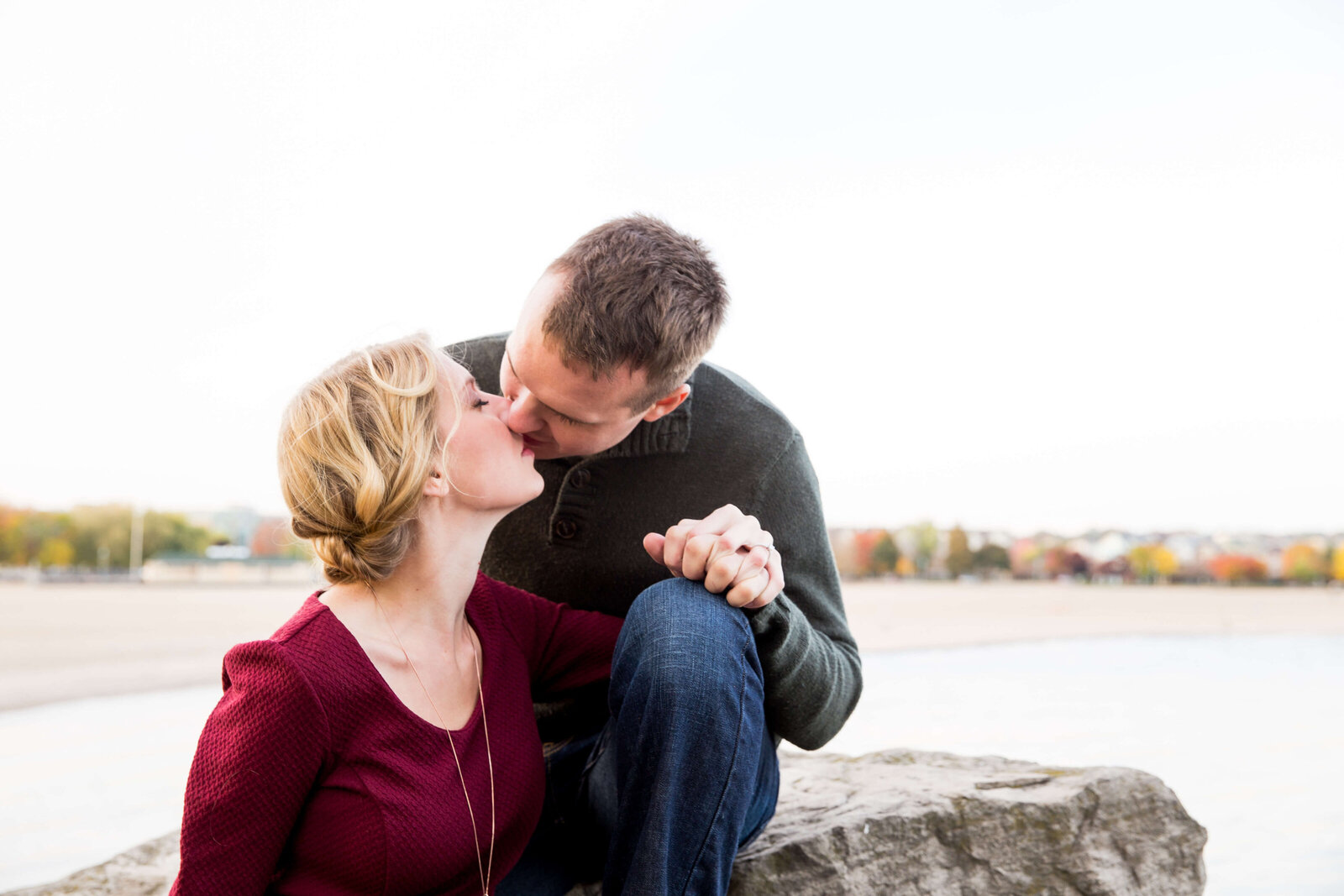 Couple kiss on rocks at Toronto beach during engagement session.