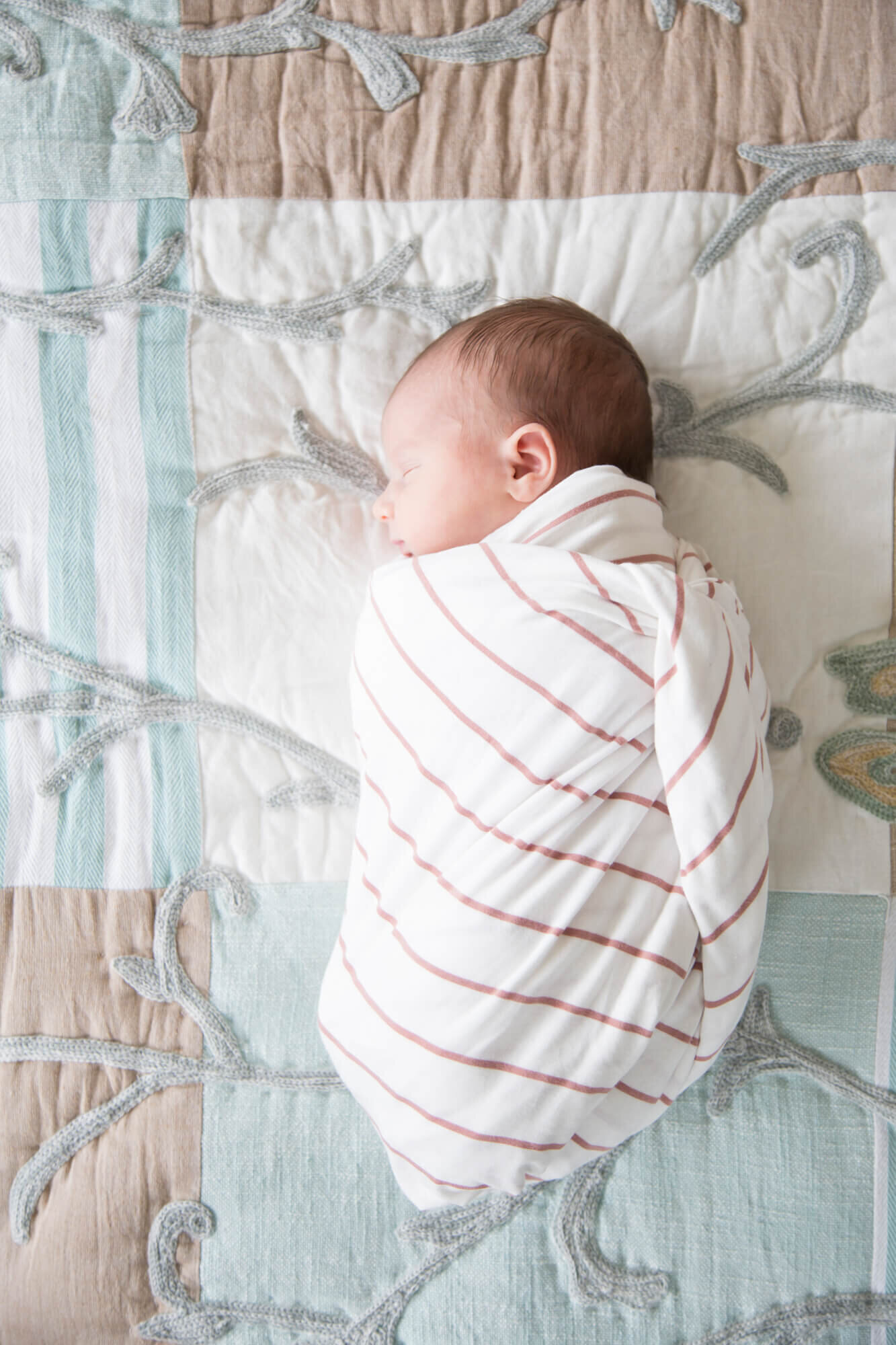 newborn baby girl laying on a bed cocooned in a swaddle