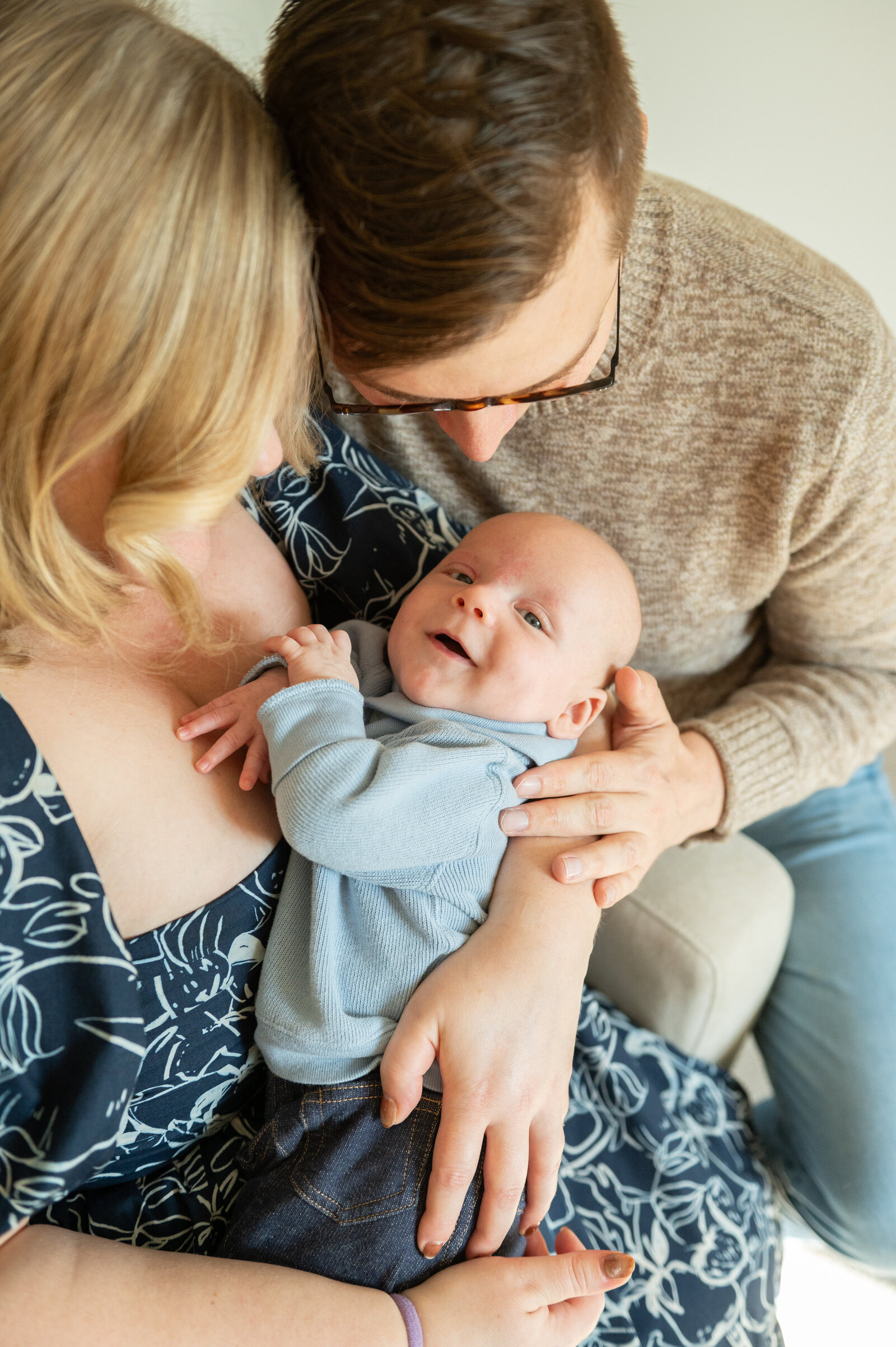 3 month old baby boy smiling at the camera while parents hold him