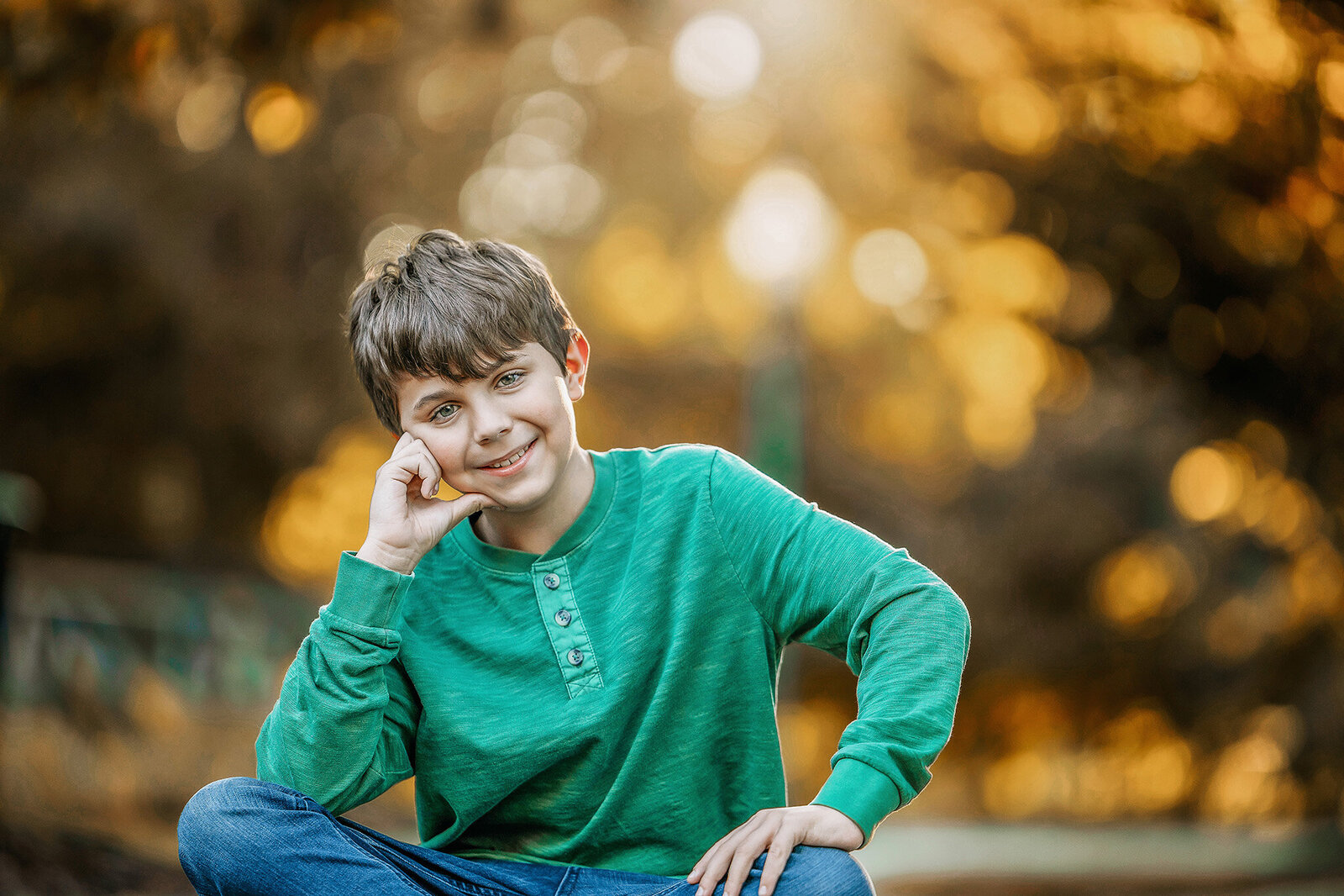 Boy sitting at the park with fall trees behind him