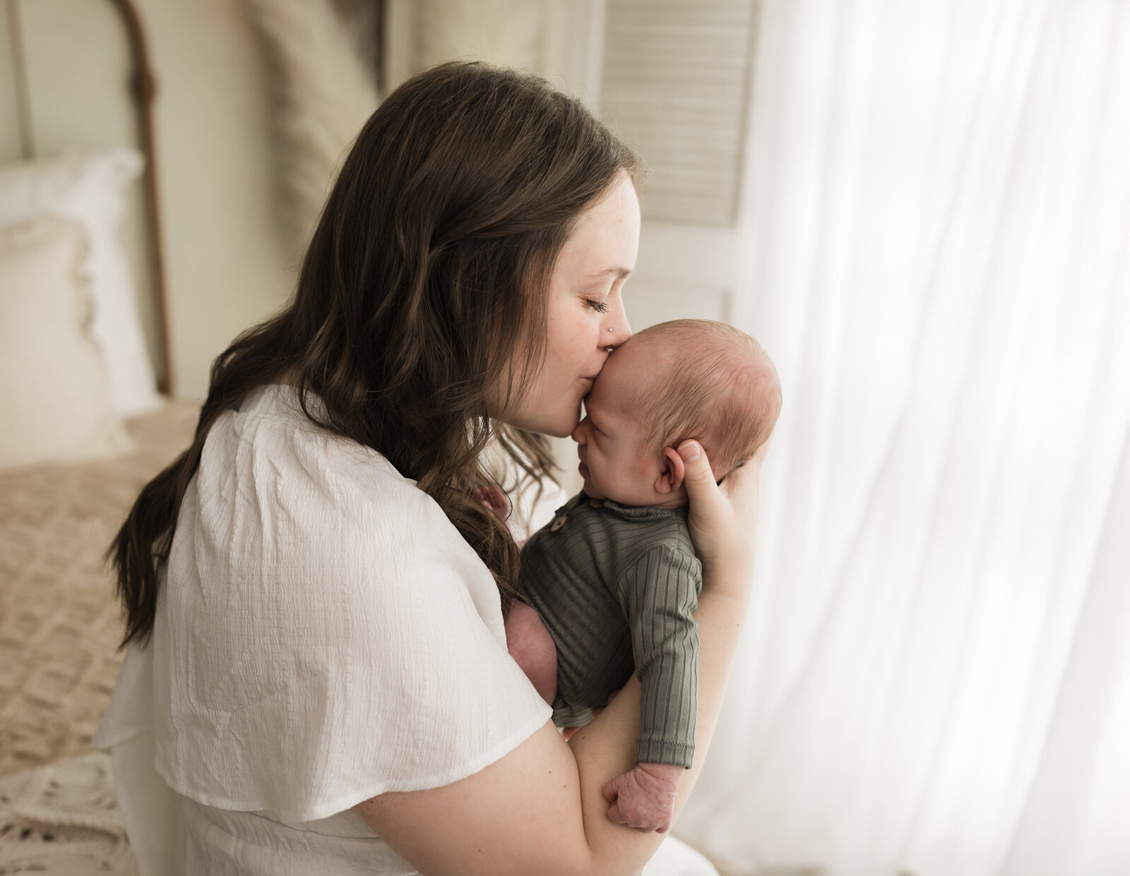 mom kissing newborn baby boy in green onesie for studio newborn photoshoot cleveland newborn photographer