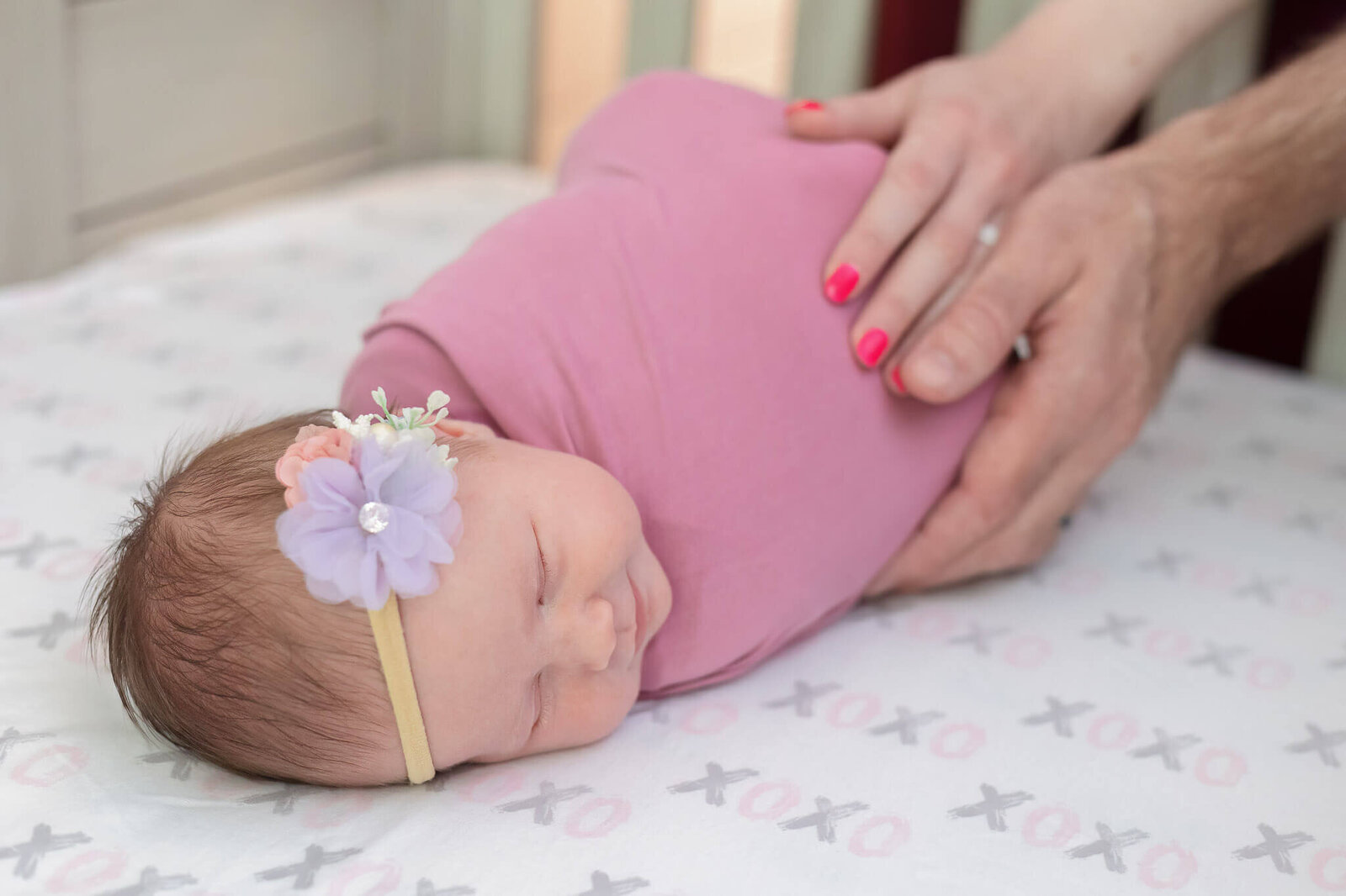 A close-up of a newborn girl wrapped in pink with mom and dad's hands on her body.