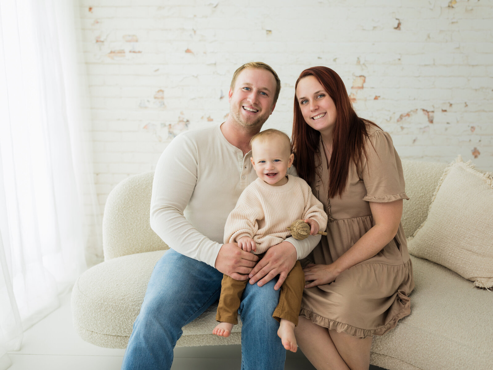 mom and dad sitting on couch with one year old son for family portraits cleveland family photography