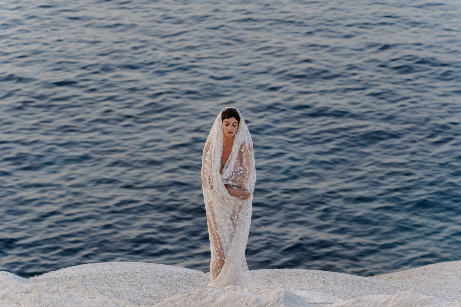 Unique, creative wedding photo of bride standing on cliff at Milos Greece