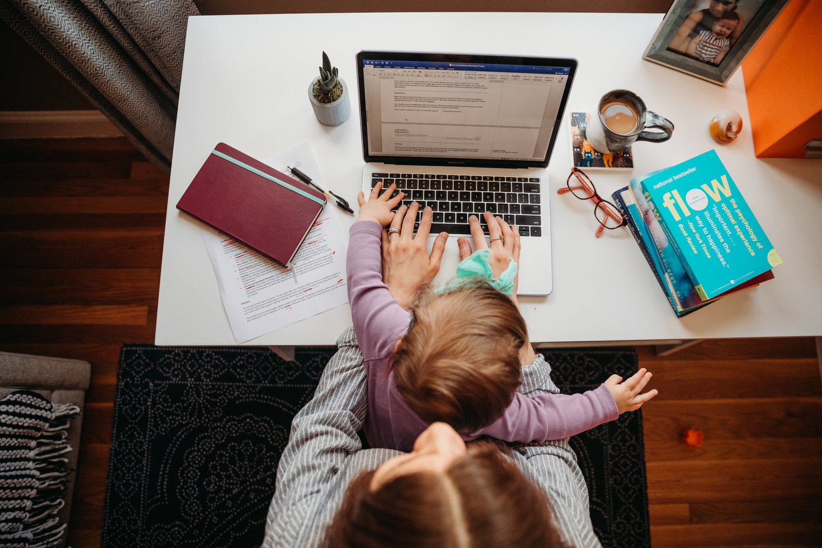 overhead shot of a female entrepreneur typing on laptop with toddler girl on lap
