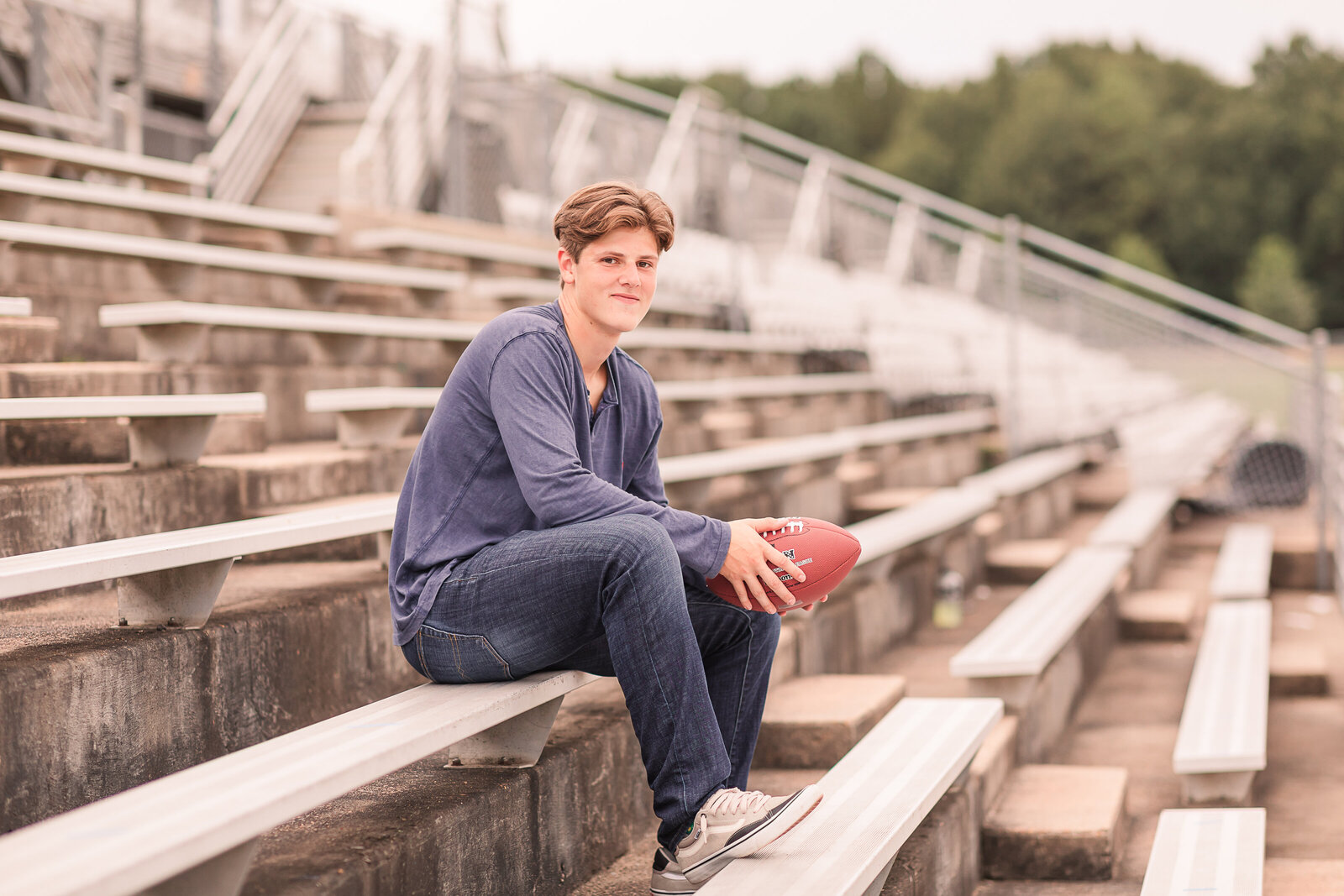 senior boy holding football on bleachers