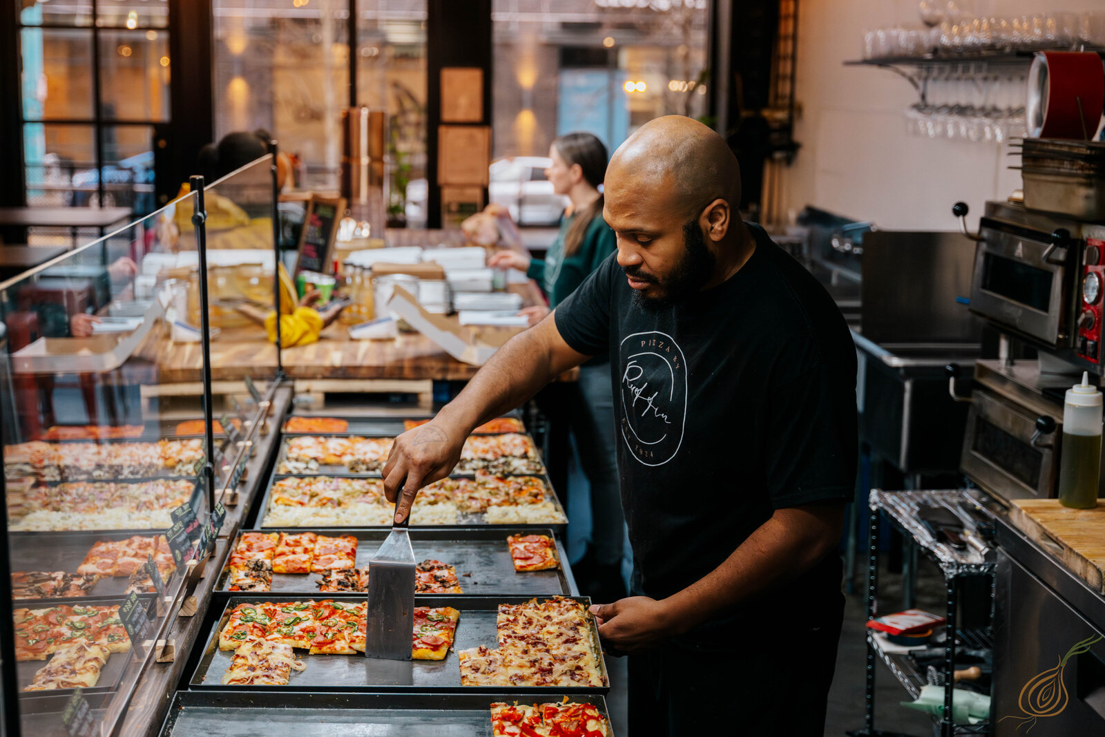 A man stands behind a counter as he serves slices of pizza. 