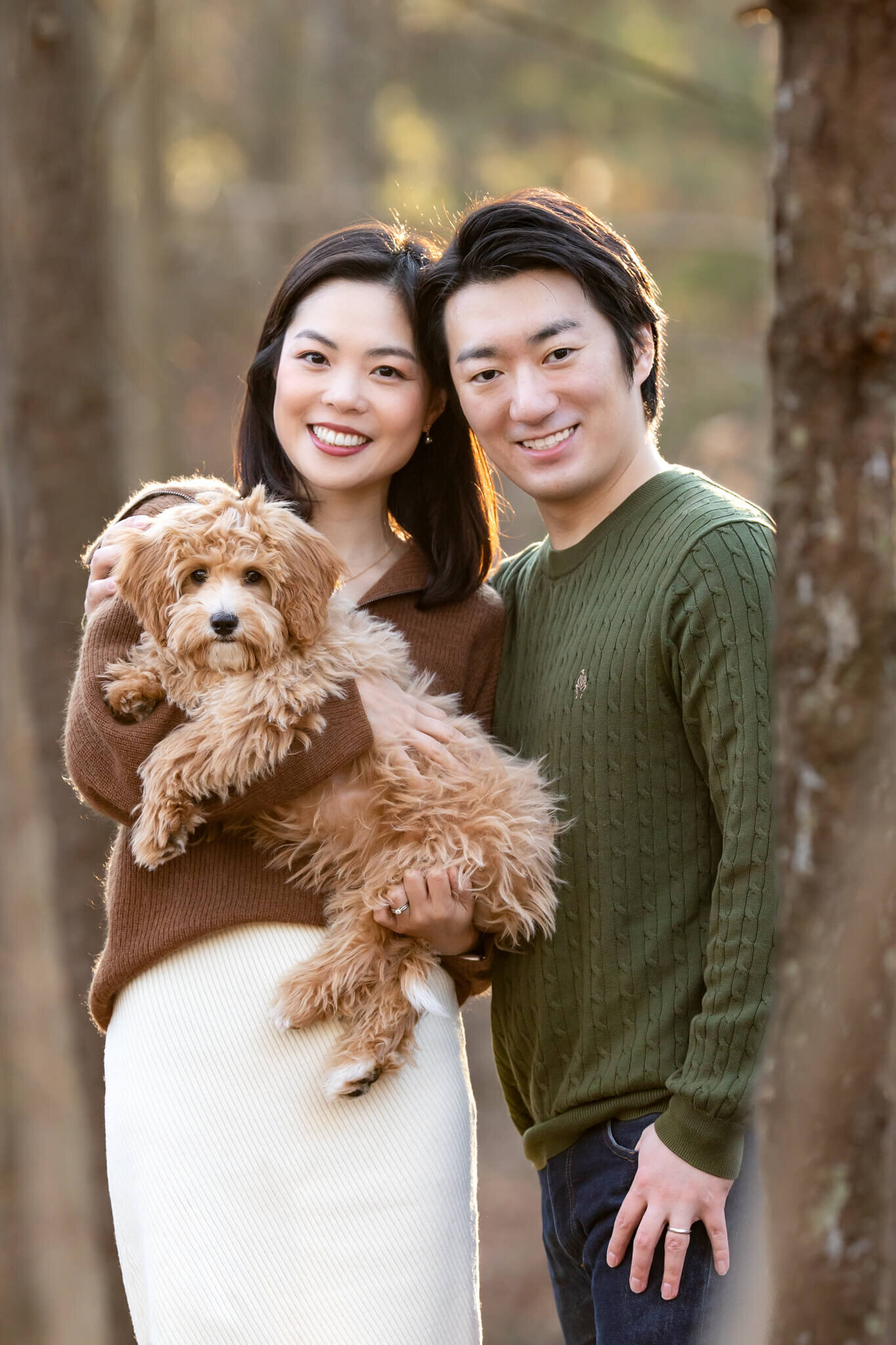 Beautiful Japanese couple  standing in the trees holding their  adorable Golden Doodle puppy