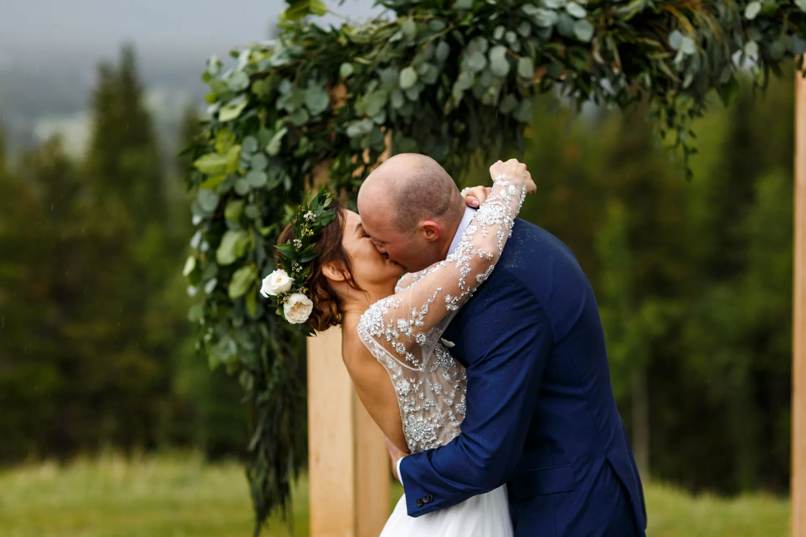 bride and groom kissing under arch in mountains