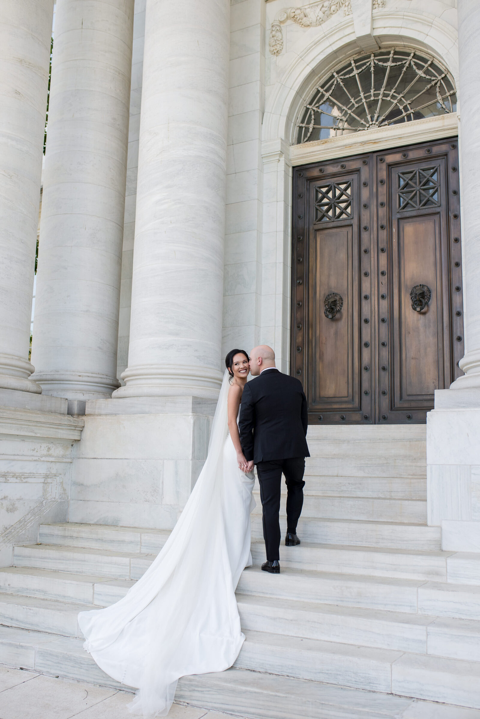 A groom kisses his bride on the steps of a church.