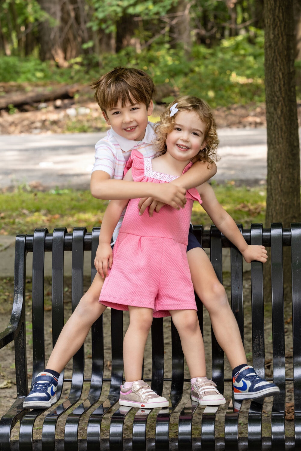 A boy and a girl are posing for a picture on a park bench